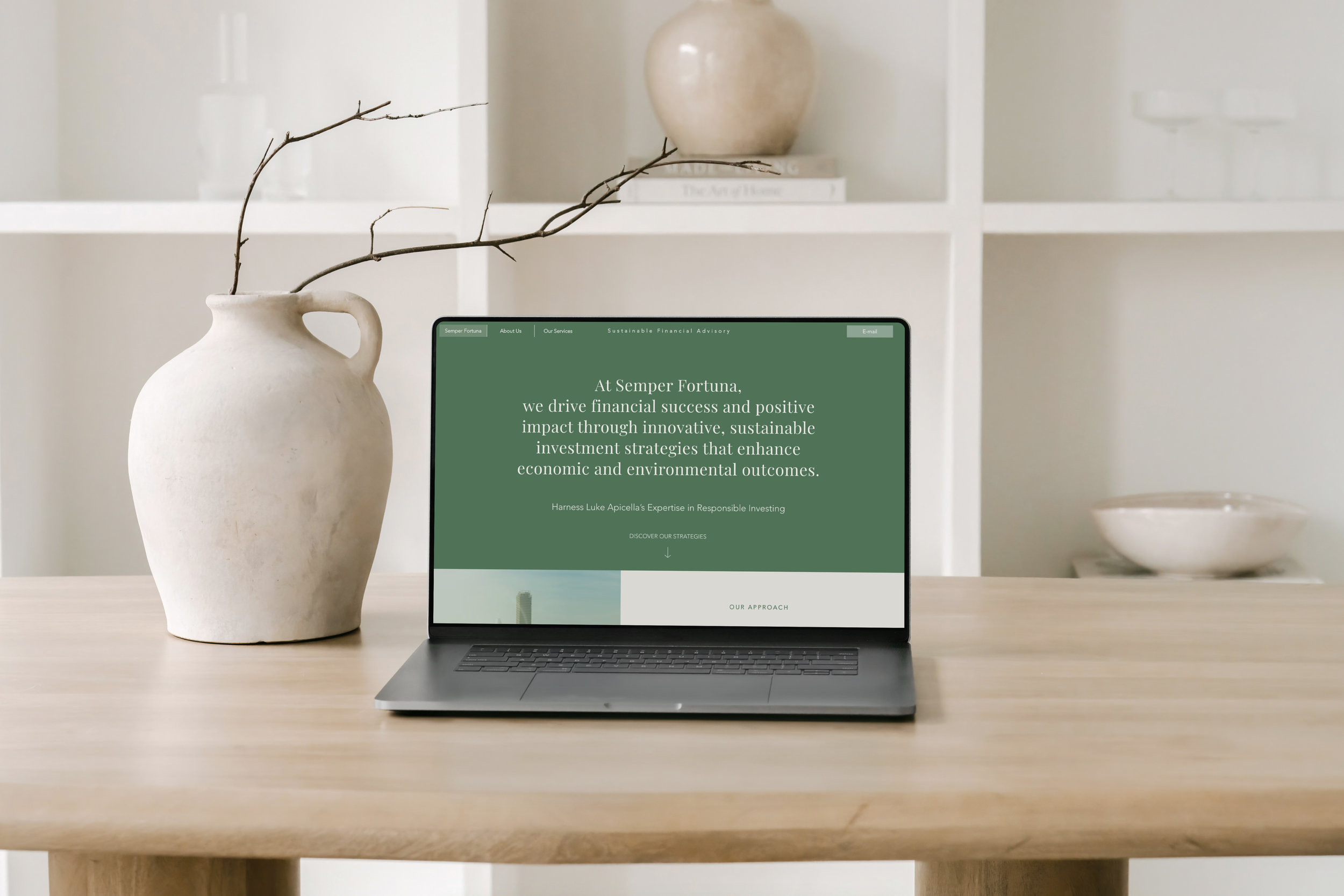 Laptop on wooden table displaying a green webpage from Semper Fortuna about financial success and sustainable investments, with a large beige vase with a branch to the left and a white shelf with decorative objects in the background.