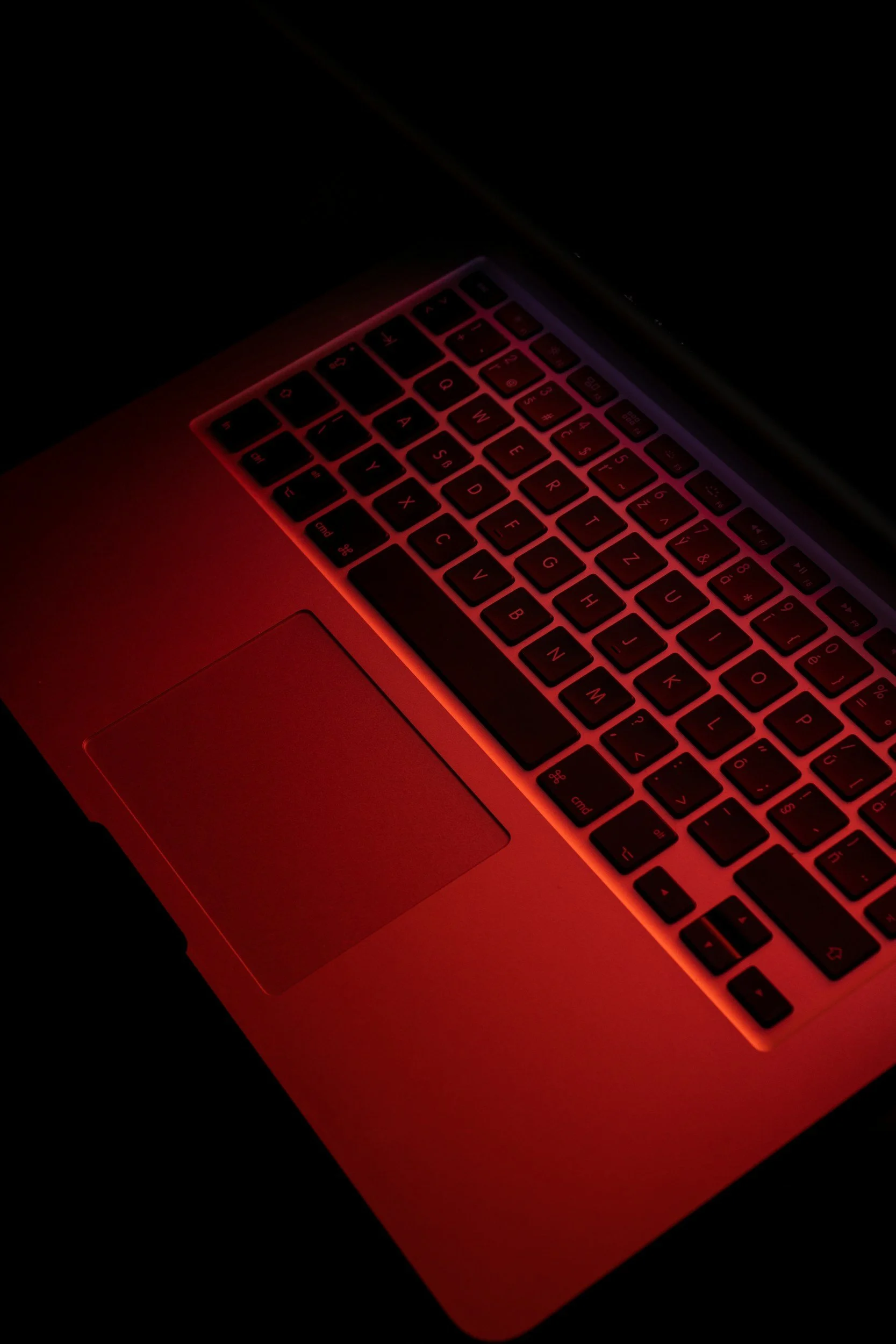 Close-up of a laptop keyboard with red backlight in a dark environment.