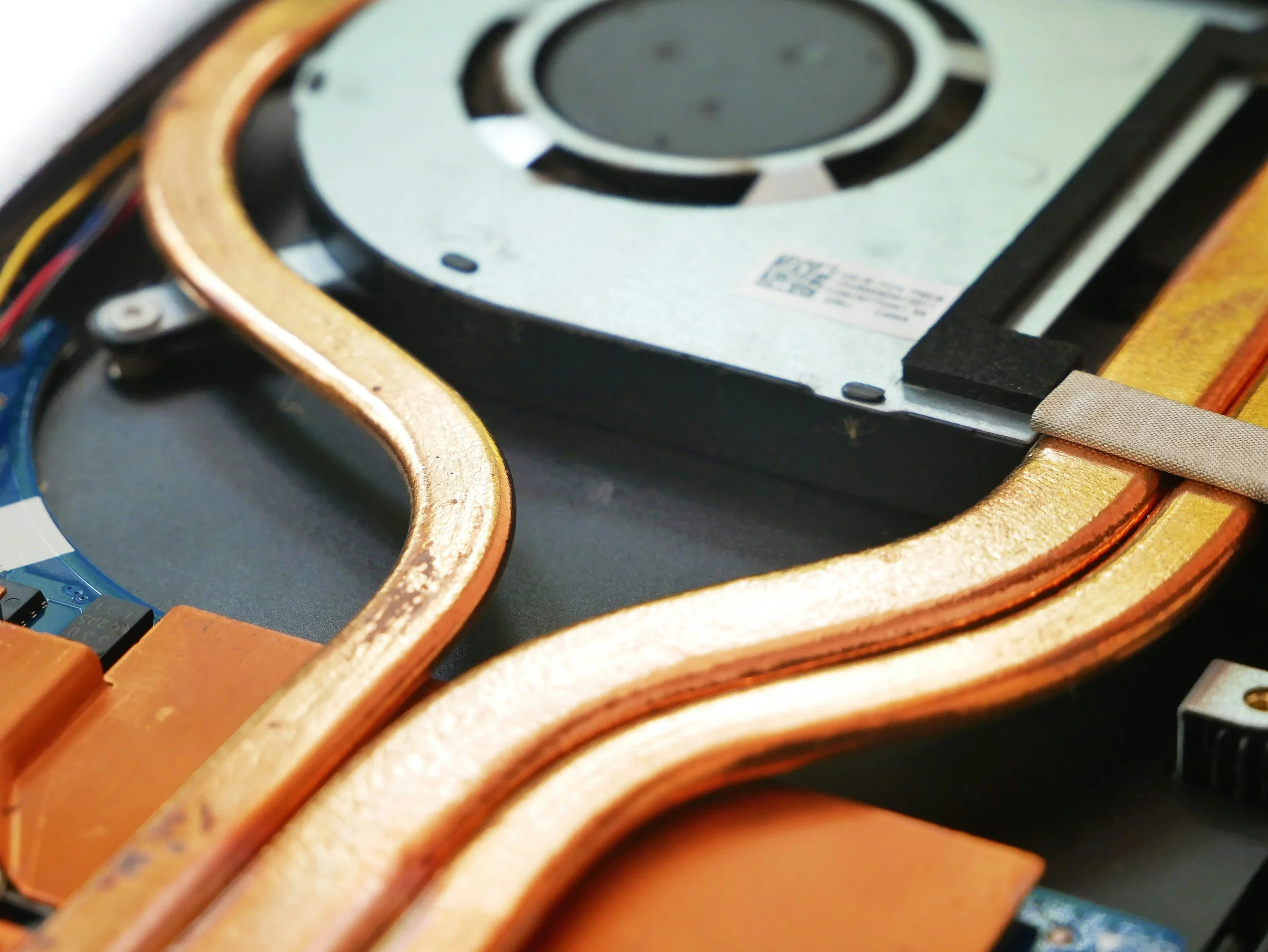 Close-up of a disassembled laptop showing copper heat pipes, cooling fan, and internal components.
