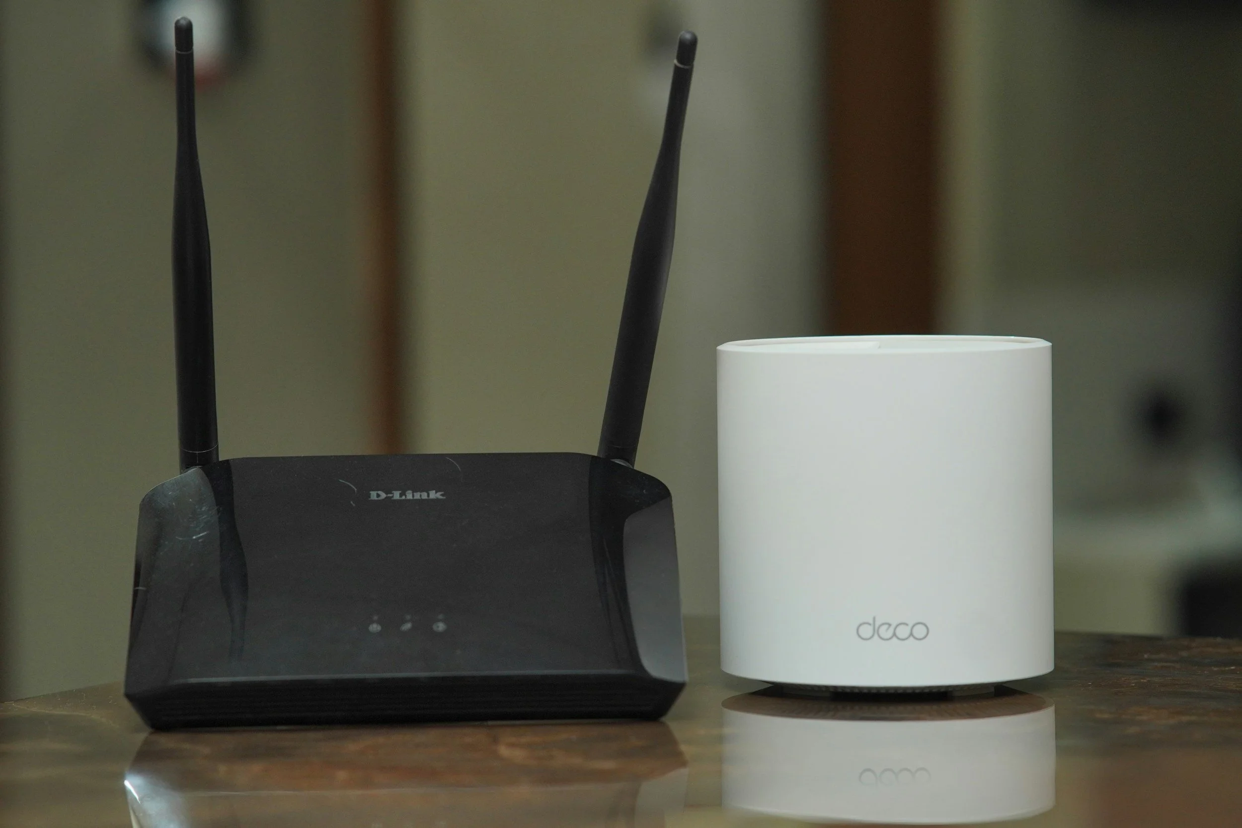 A black D-Link wireless router with two antennas and a white Decco smart home device on a wooden surface.