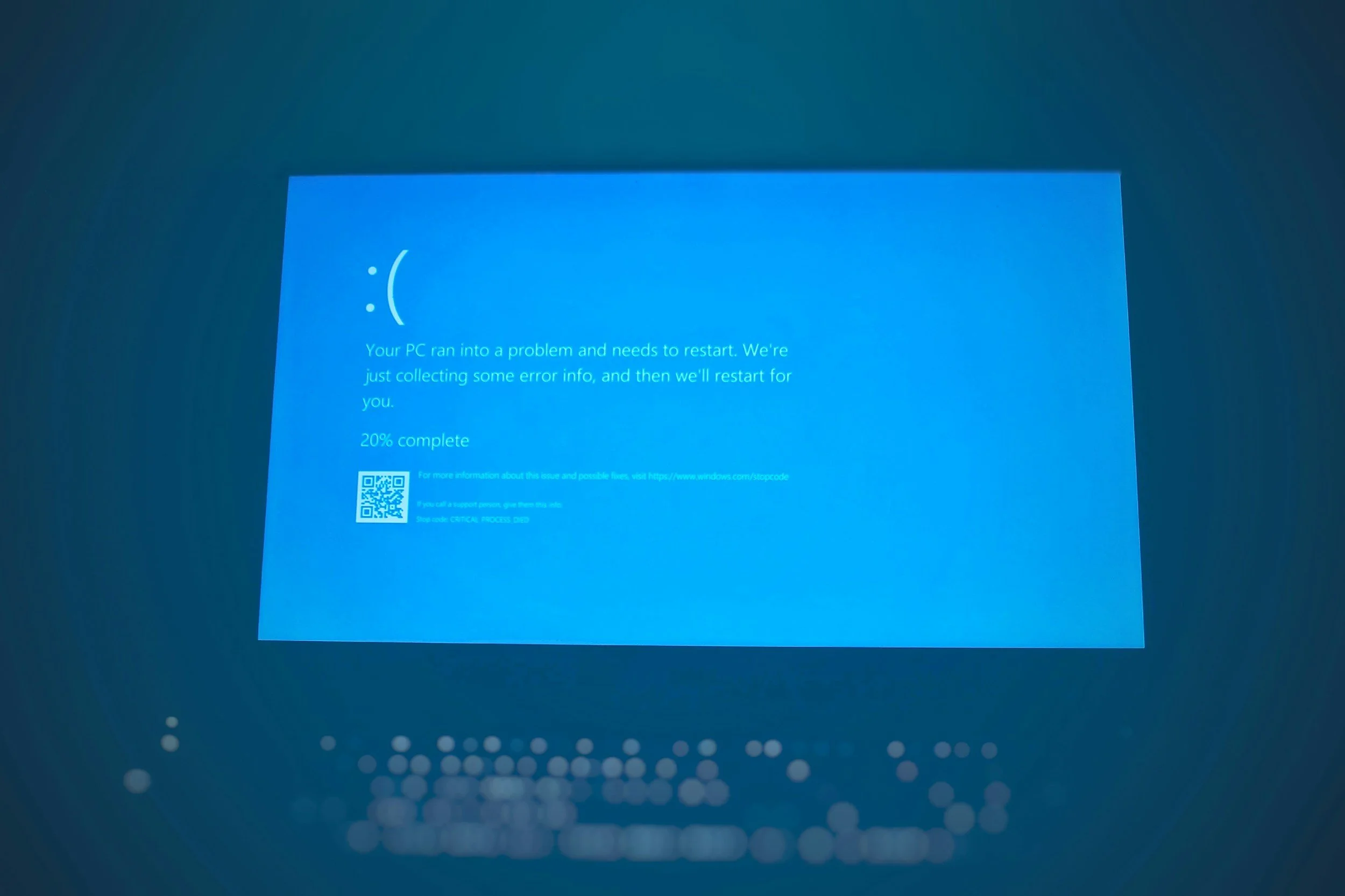 Windows blue error screen indicating a system problem, with a sad face emoticon, text about a PC needing to restart, and a QR code at the bottom left.