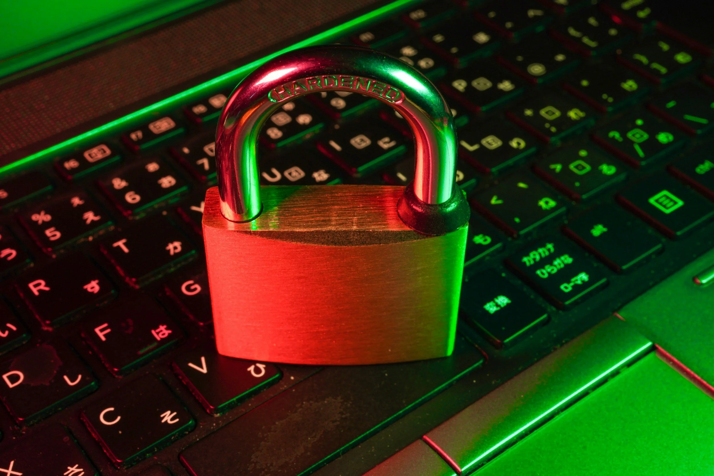 A silver padlock with a shiny metallic finish placed on a black computer keyboard illuminated with red and green lights.