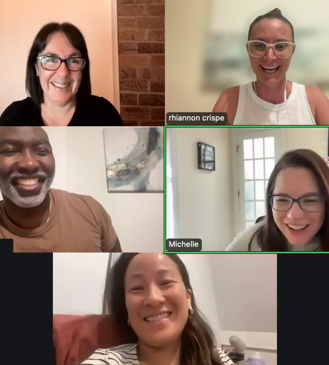 Six people in a video call, all smiling and looking at their screens. Four women and one man are visible, with name labels for Rhiannon Crispe and Michelle. The background varies, including a brick wall, a window, and artwork.