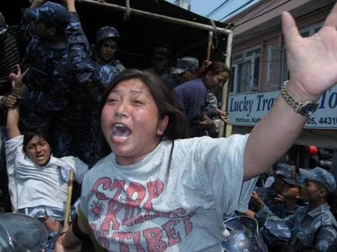 Picture from Human Rights Watch Report of Tibetans in Nepal being dragged away by police. Woman in the foreground is screaming and wears a hand-drawn shirt that says Stop the Killing in Tibet