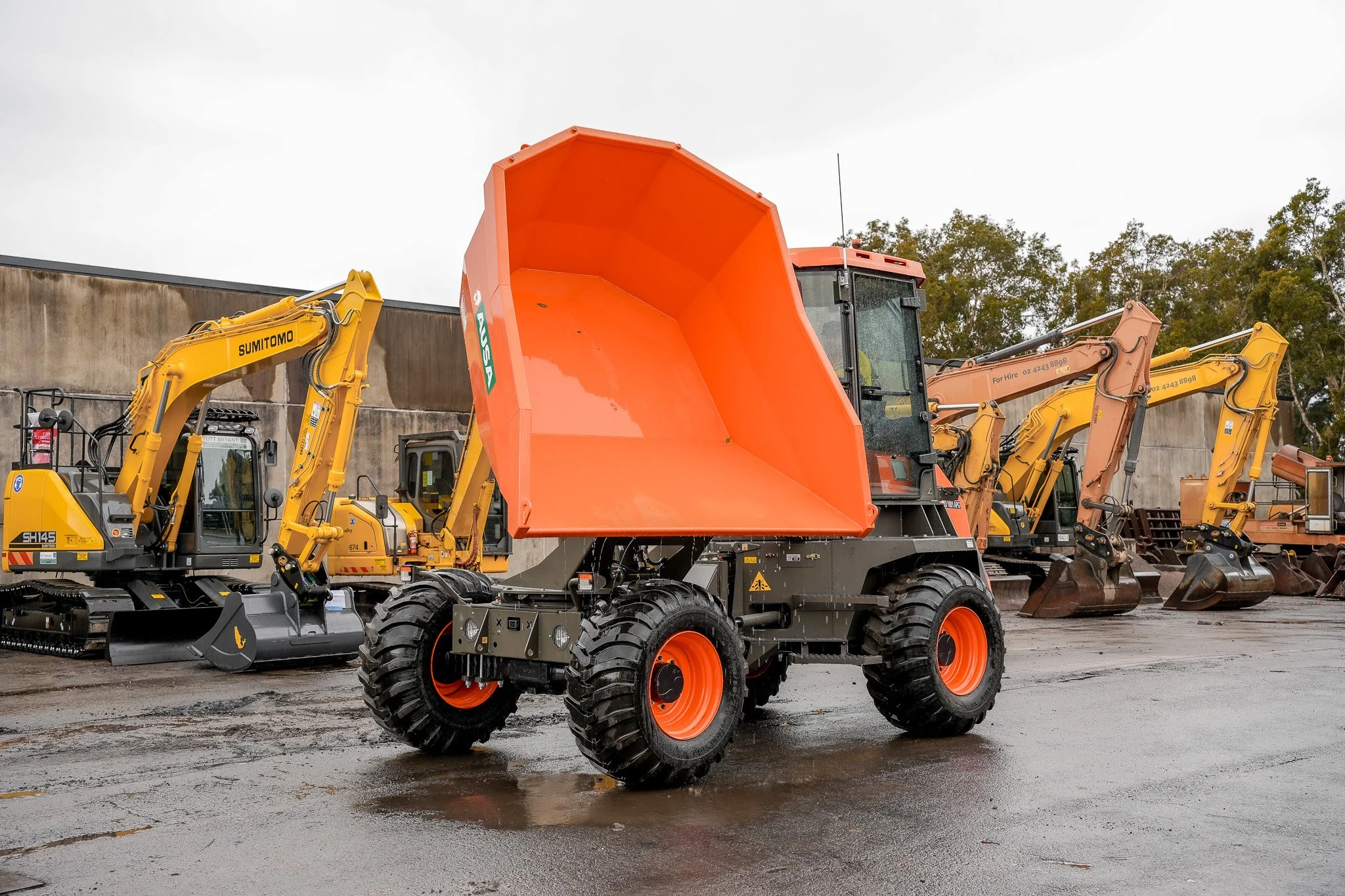 Construction equipment yard with a front loader and excavators parked on wet pavement.