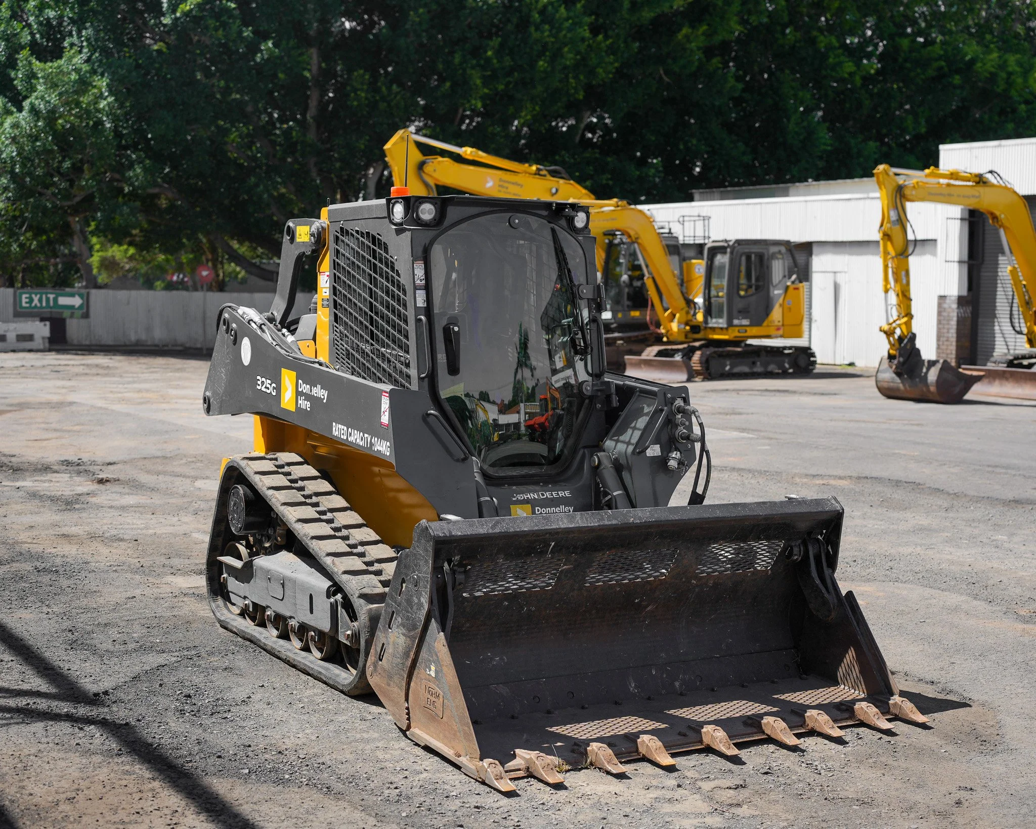 Construction site with a John Deere compact track loader in the foreground and multiple excavators parked in the background.