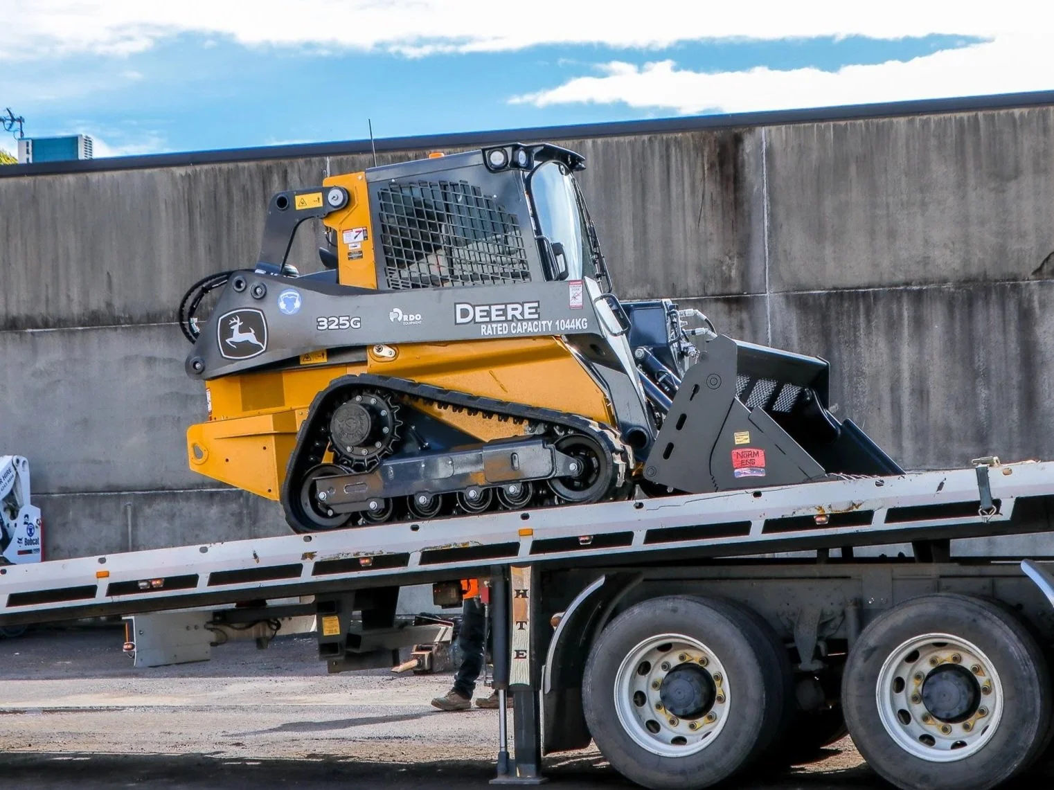 A compact bulldozer with tracks and a large metal blade at the front, parked on a gravel surface with construction machinery in the background.