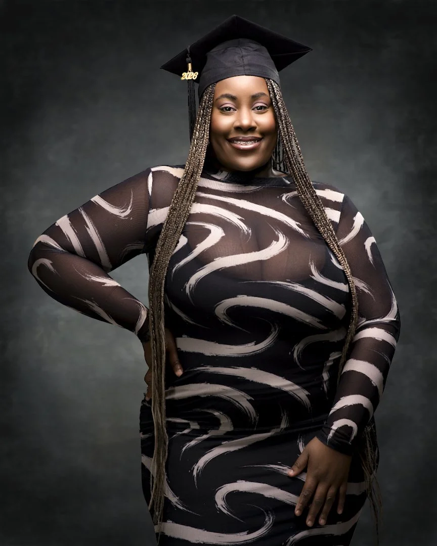 A woman celebrating graduation, wearing a black gown and cap with a tassel that reads '2024'. She has long braided hair and is smiling at the camera with a hand on her hip.