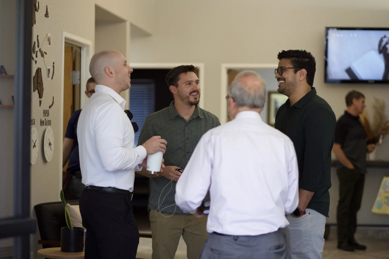 Four men in conversation inside the church lobby, with a TV on the wall and decorative clocks.