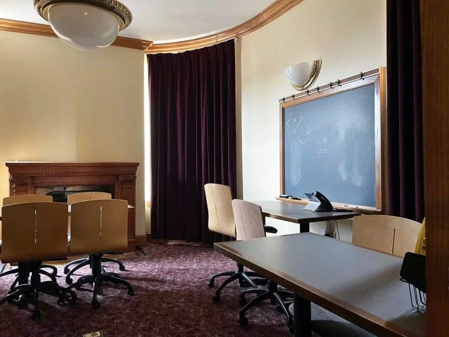 A conference room with a blackboard, chairs, a desk, a telephone, and dark curtains.