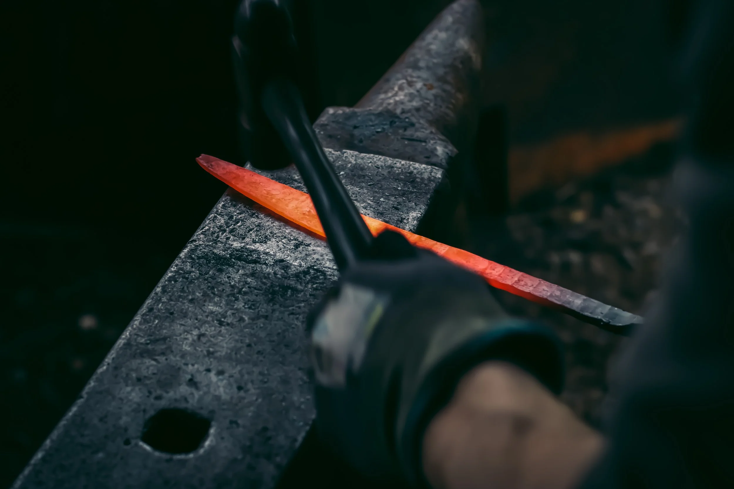 Blacksmith shaping a glowing hot piece of metal on an anvil.