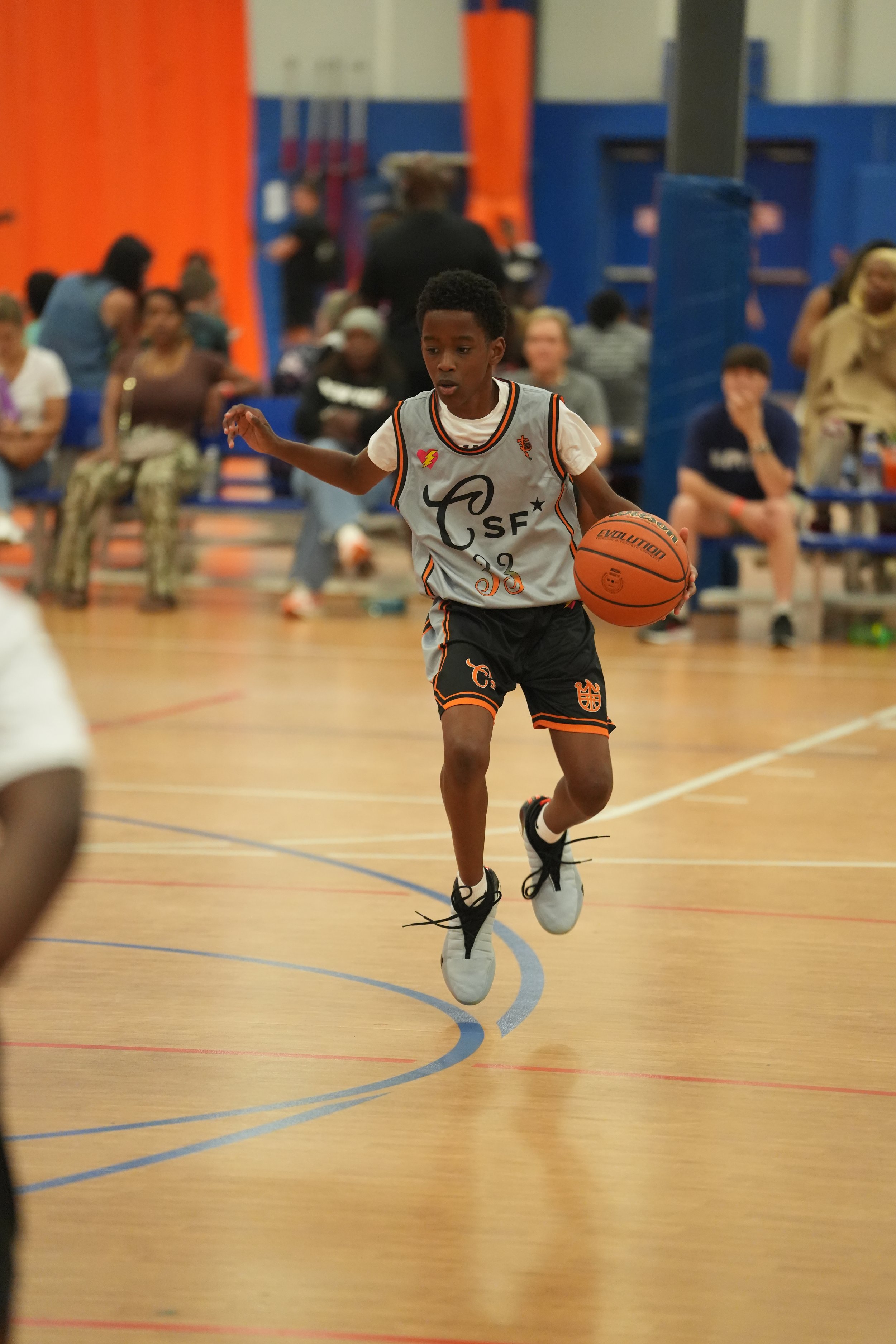 Young boy playing basketball on an indoor court, wearing a white and black jersey with the number 33, dribbling the ball.