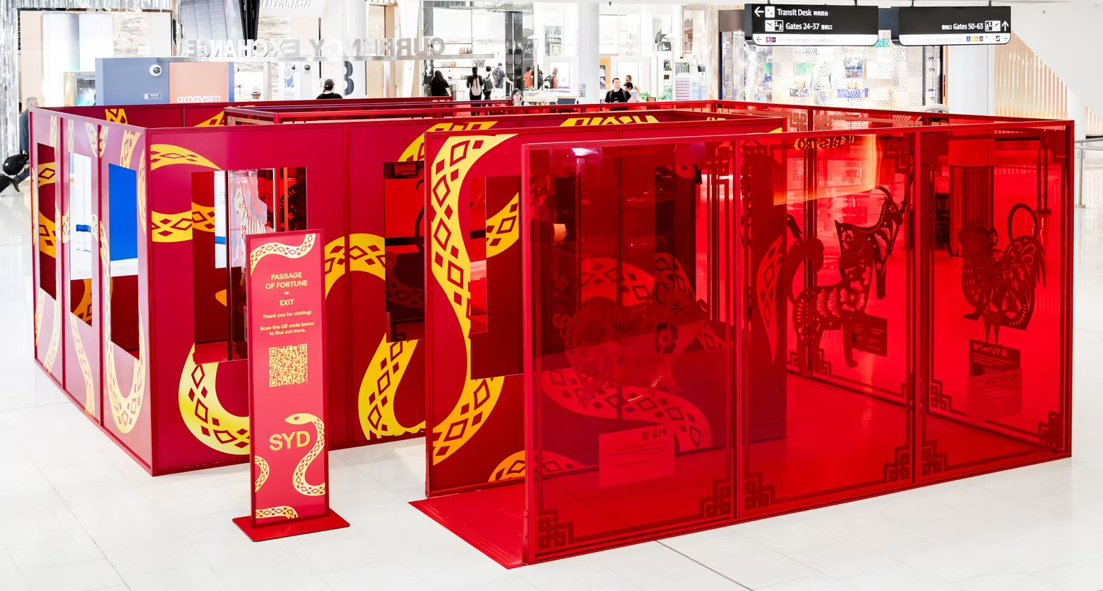 A colorful maze display at an indoor shopping mall with red panels decorated with yellow dragon designs, labeled as 'Passage of Fortune,' featuring an exit sign, and directions for gates 24-37 and 50-63.