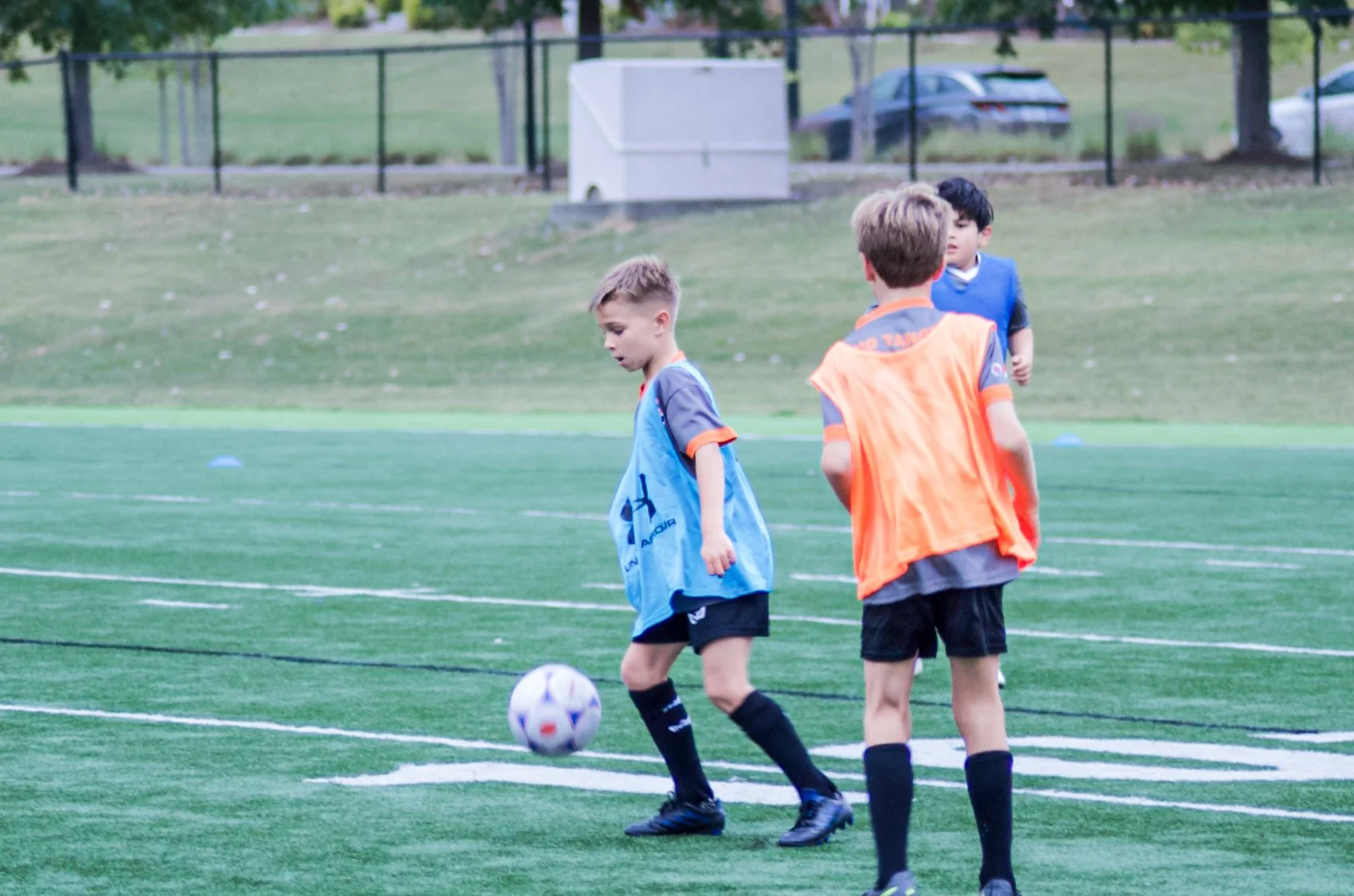 Young boys playing soccer on a field, with some boys wearing orange and blue pinnies.