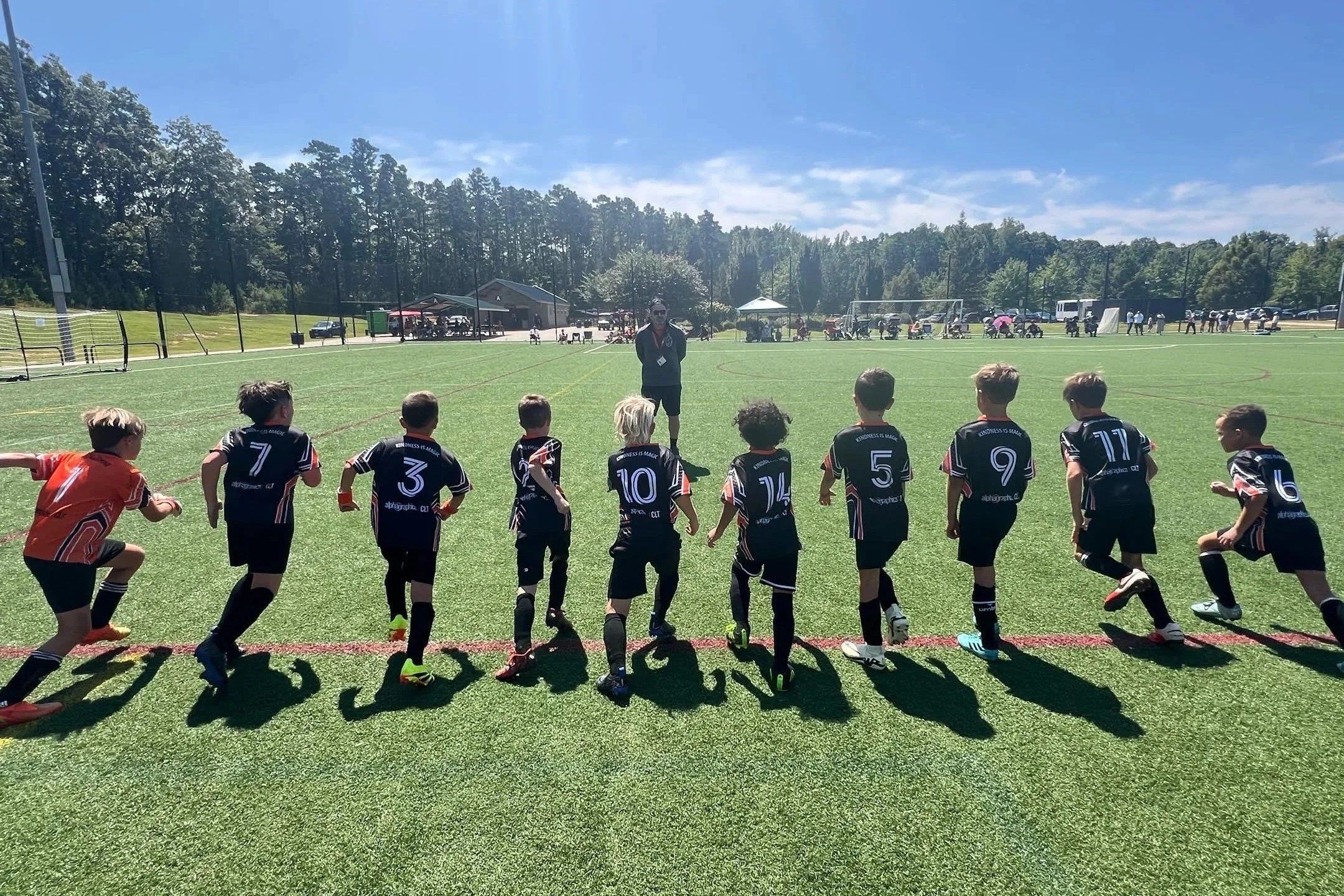 Young soccer players in black uniforms during a game on a green field on a sunny day.