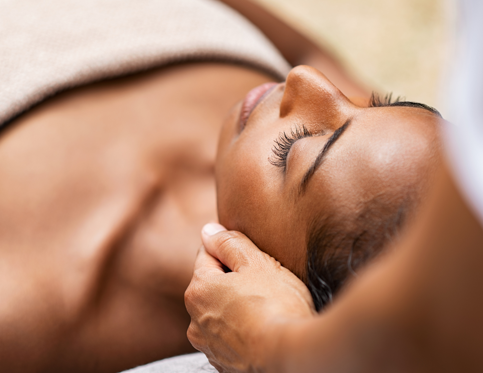 A woman receiving a facial massage while lying down with eyes closed.
