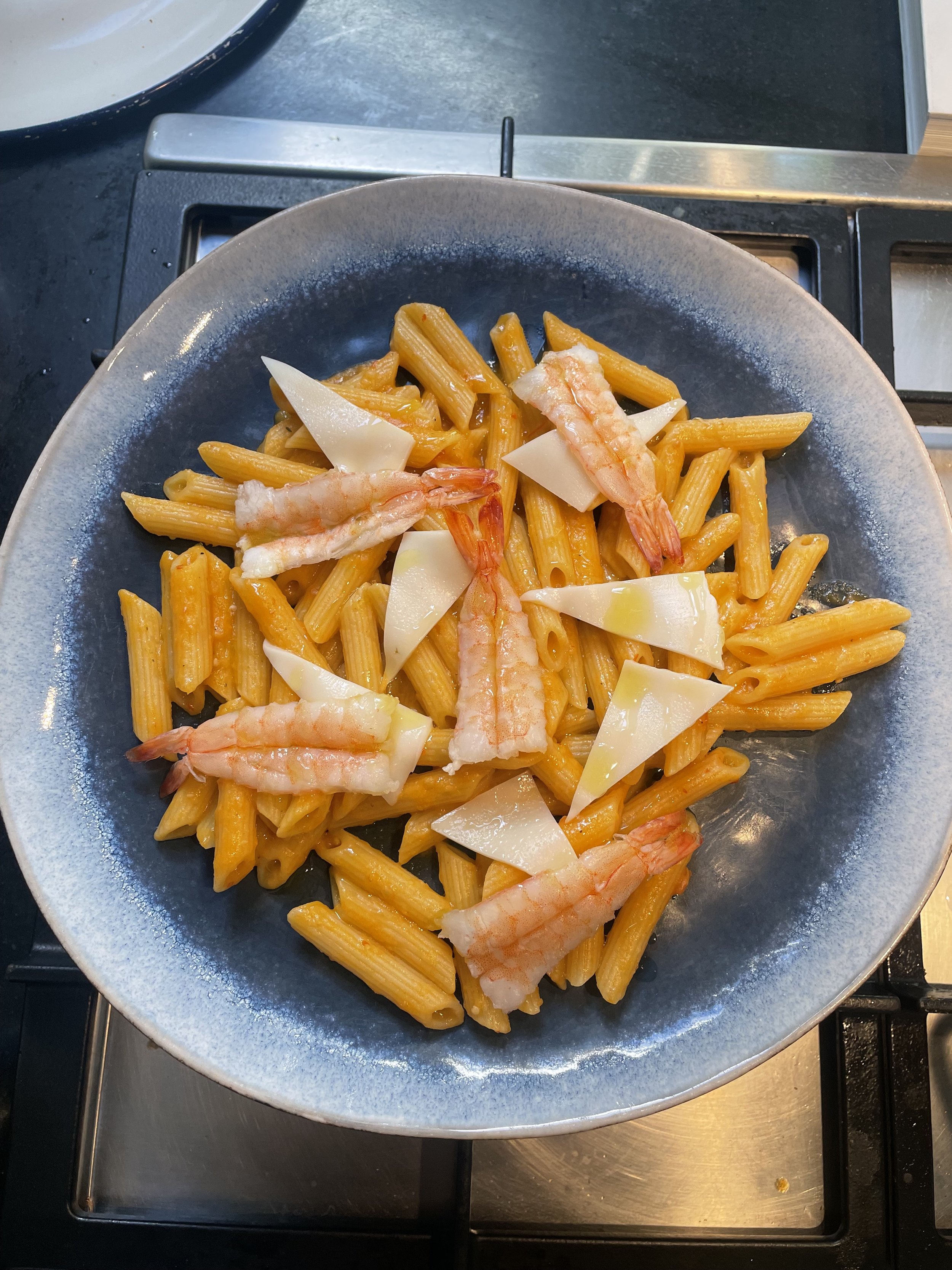 Pasta with shrimp and cheese on a gray plate, placed on a stove burner.