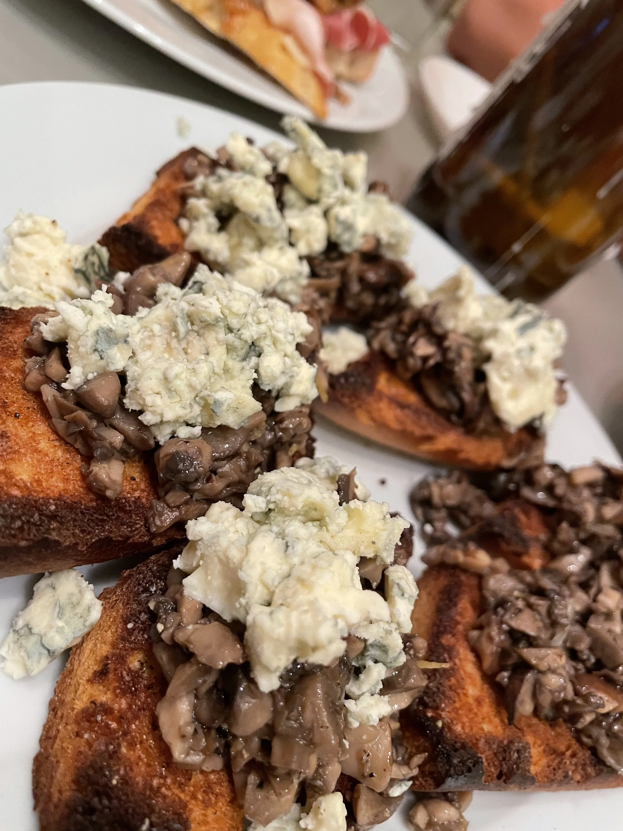Close-up of buffalo chicken wings topped with blue cheese crumbles and chopped mushrooms, served on a white plate.