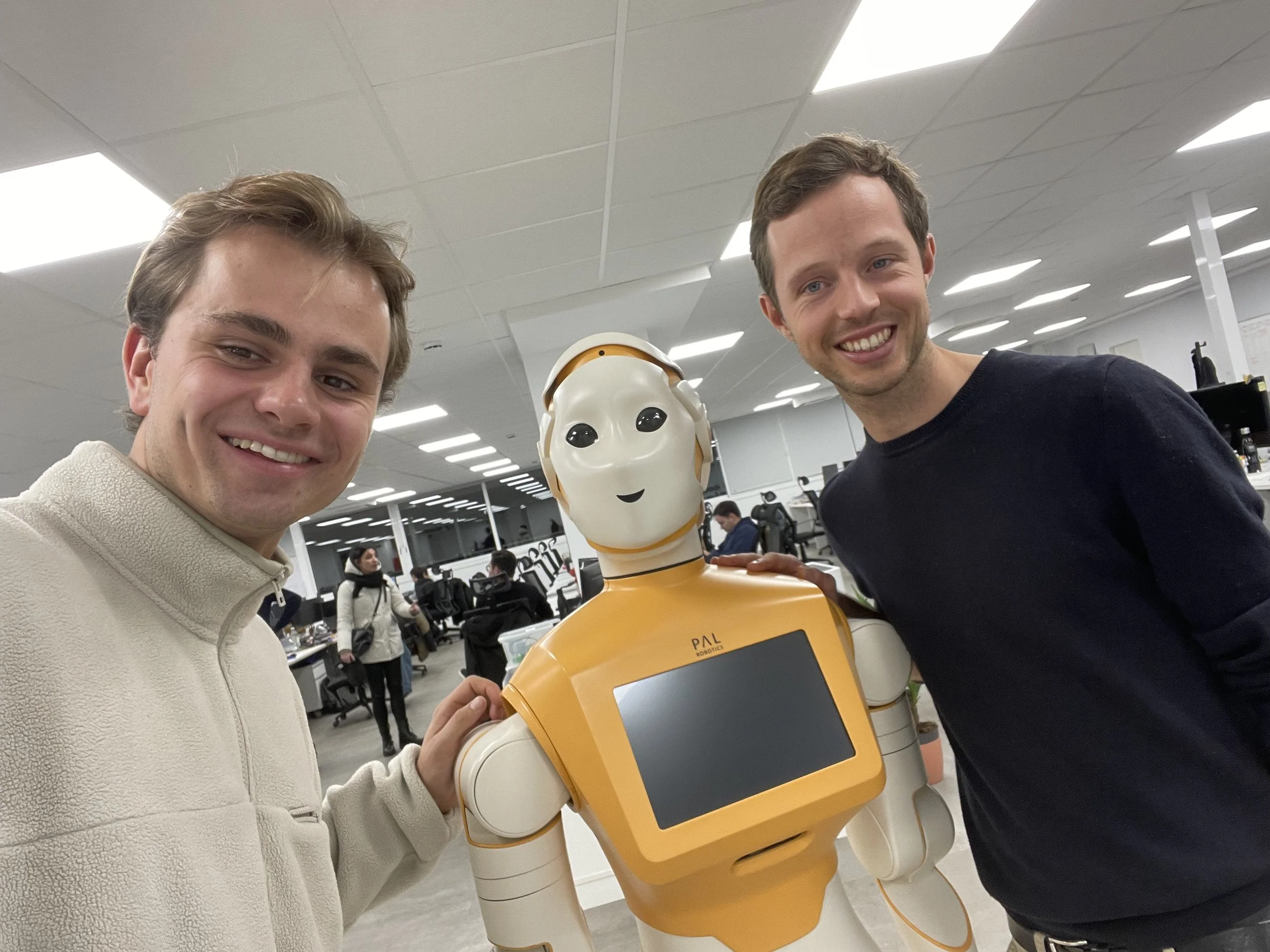 Two smiling men posing with a friendly robot in an office setting.
