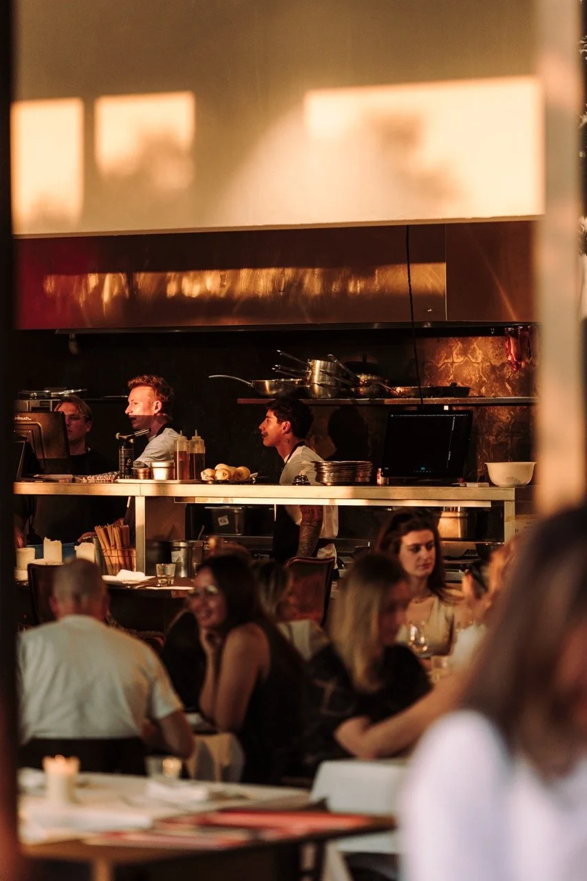 People dining inside a restaurant with a visible open kitchen in the background.