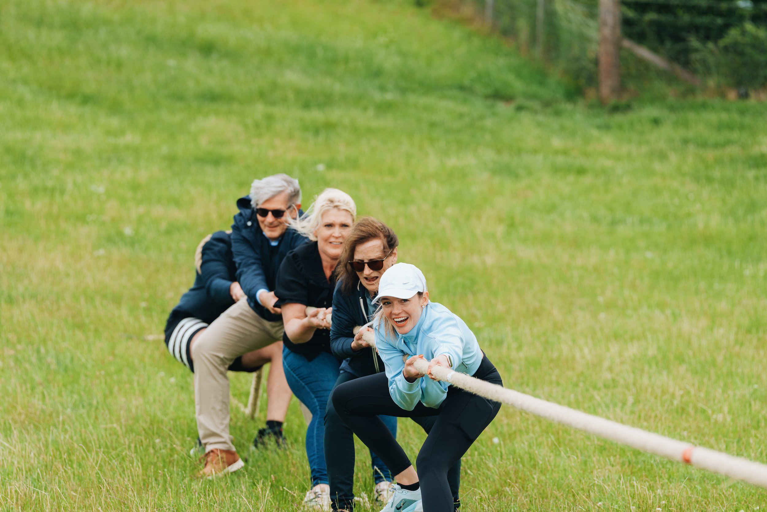 A group of people participating in a game of tug-of-war on a grassy field, pulling on a rope with determined expressions.