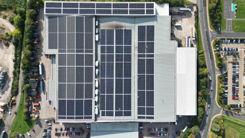 Aerial view of a large commercial building with multiple solar panel arrays on its roof, surrounded by parking lots and green landscaping.