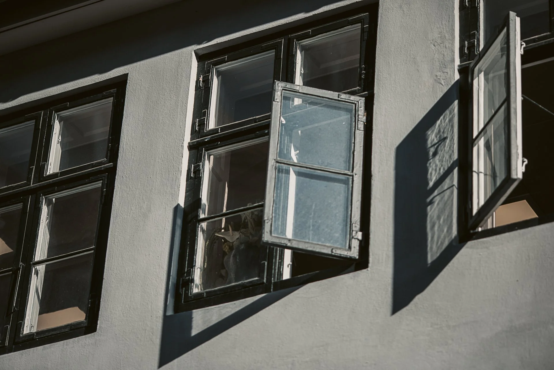 Fenster an einer Hausfassade mit geöffnetem oberen Fensterflügel, Schatten des Fensters auf die Wand