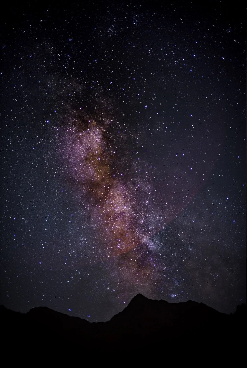 Sternenhimmel mit der Milchstraße über dunklen Bergen bei Nacht.