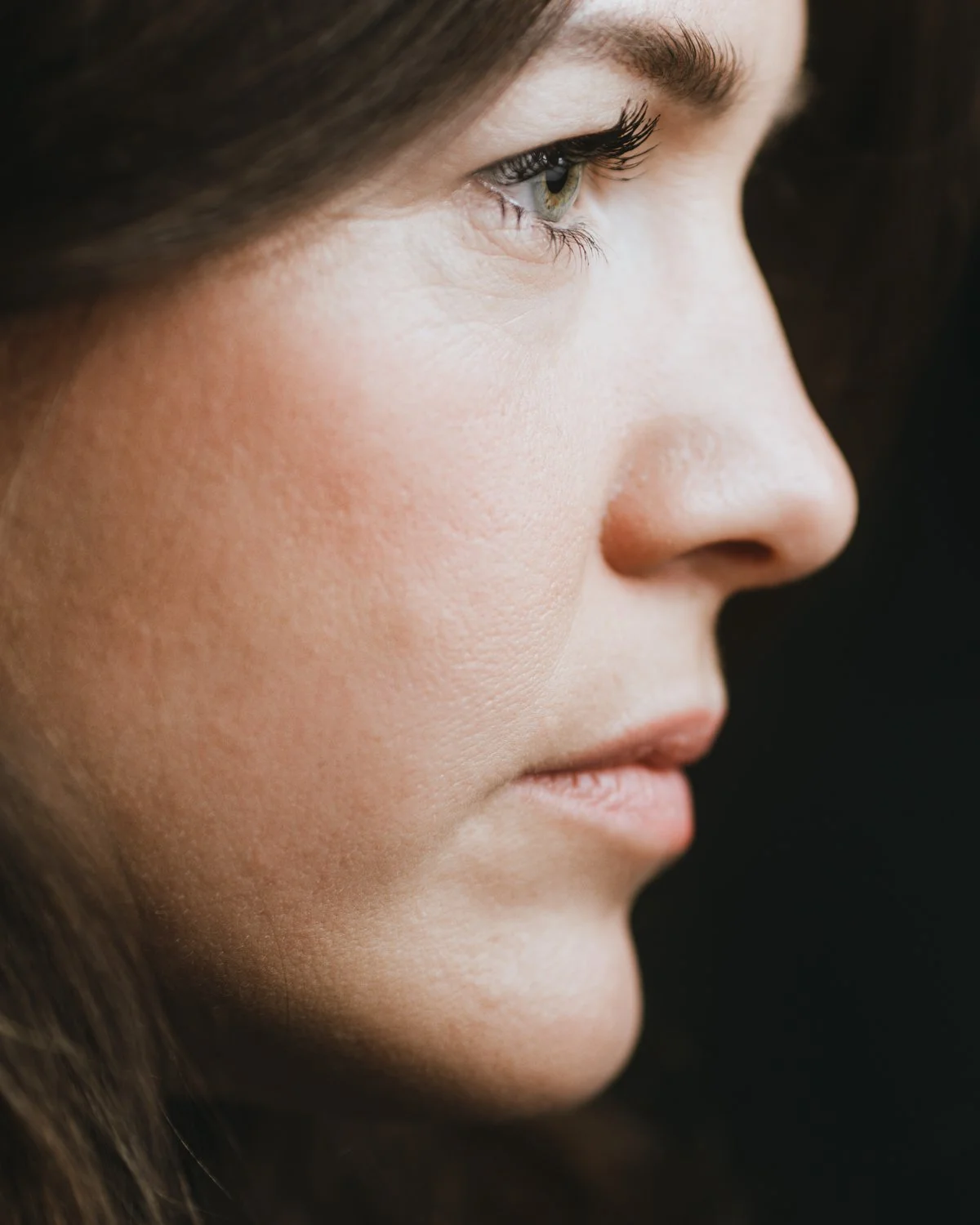 Nahaufnahme eines Frauenprofils mit braunen Haaren, grünen Augen und natürlichem Make-up.