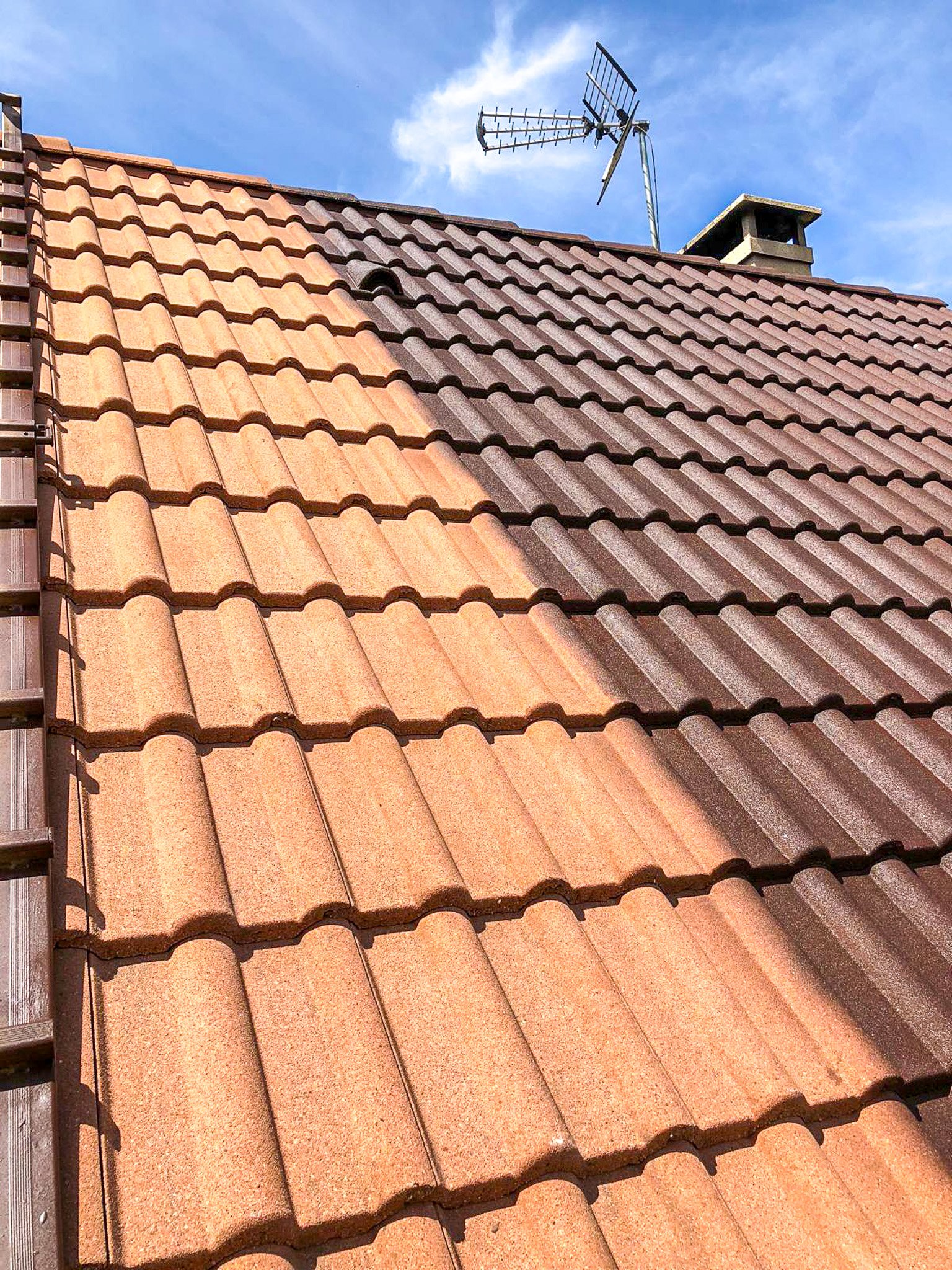 Toit en tuiles en terre cuite orangées avec un antenne parabolique et une cheminée contre un ciel bleu avec quelques nuages.