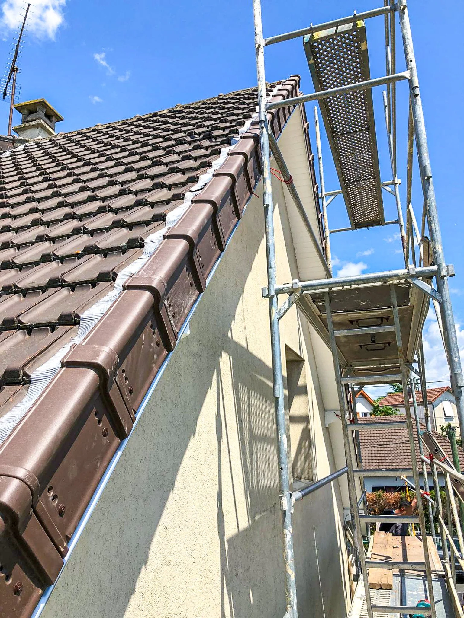 Échafaudage à côté d'un toit en tuiles brunes d'une maison en cours de rénovation ou d'entretien.