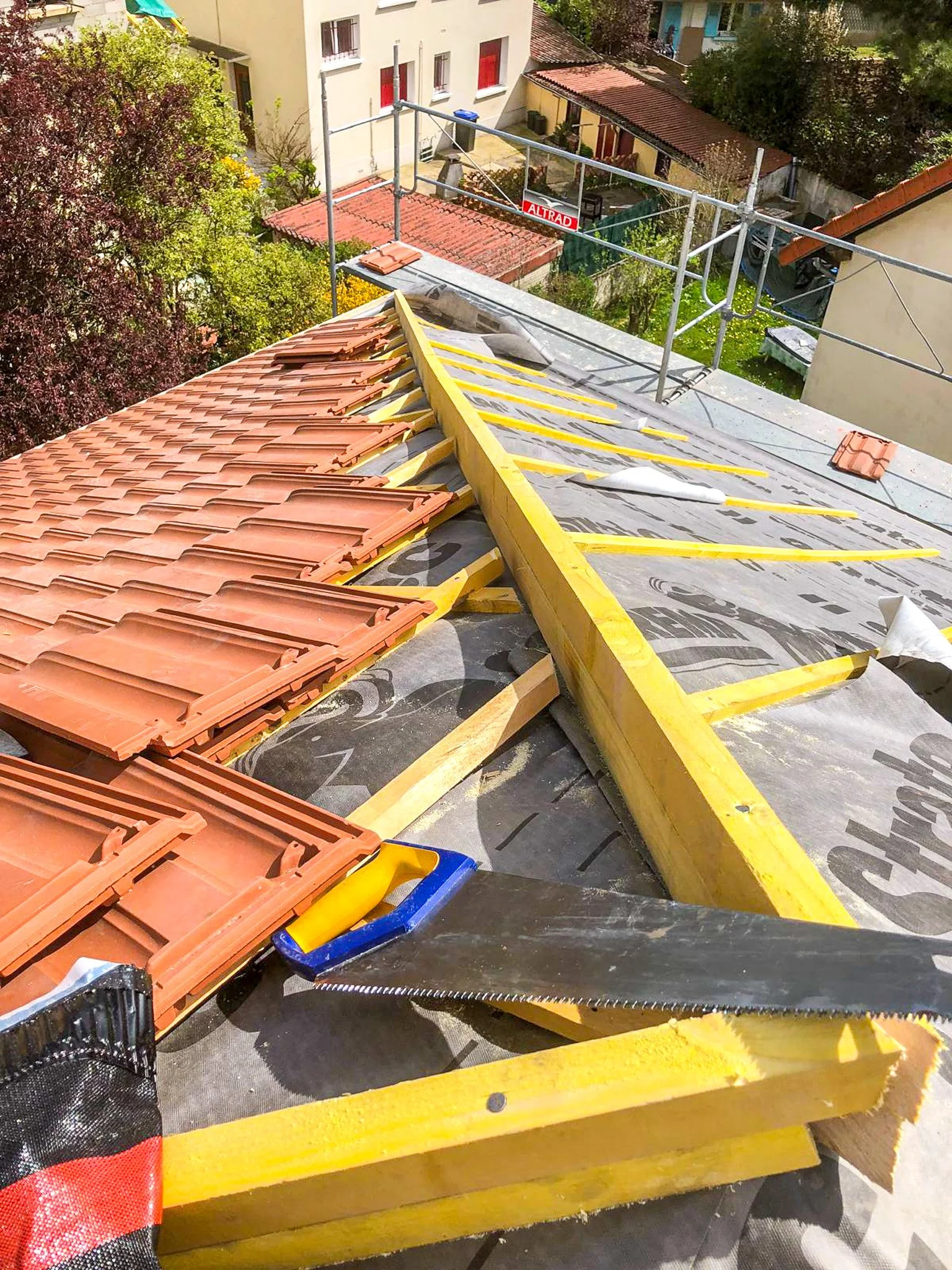 Travaux de toiture en cours, pose de tuiles en terre cuite sur la toiture d'une maison, échafaudages autour du bâtiment.