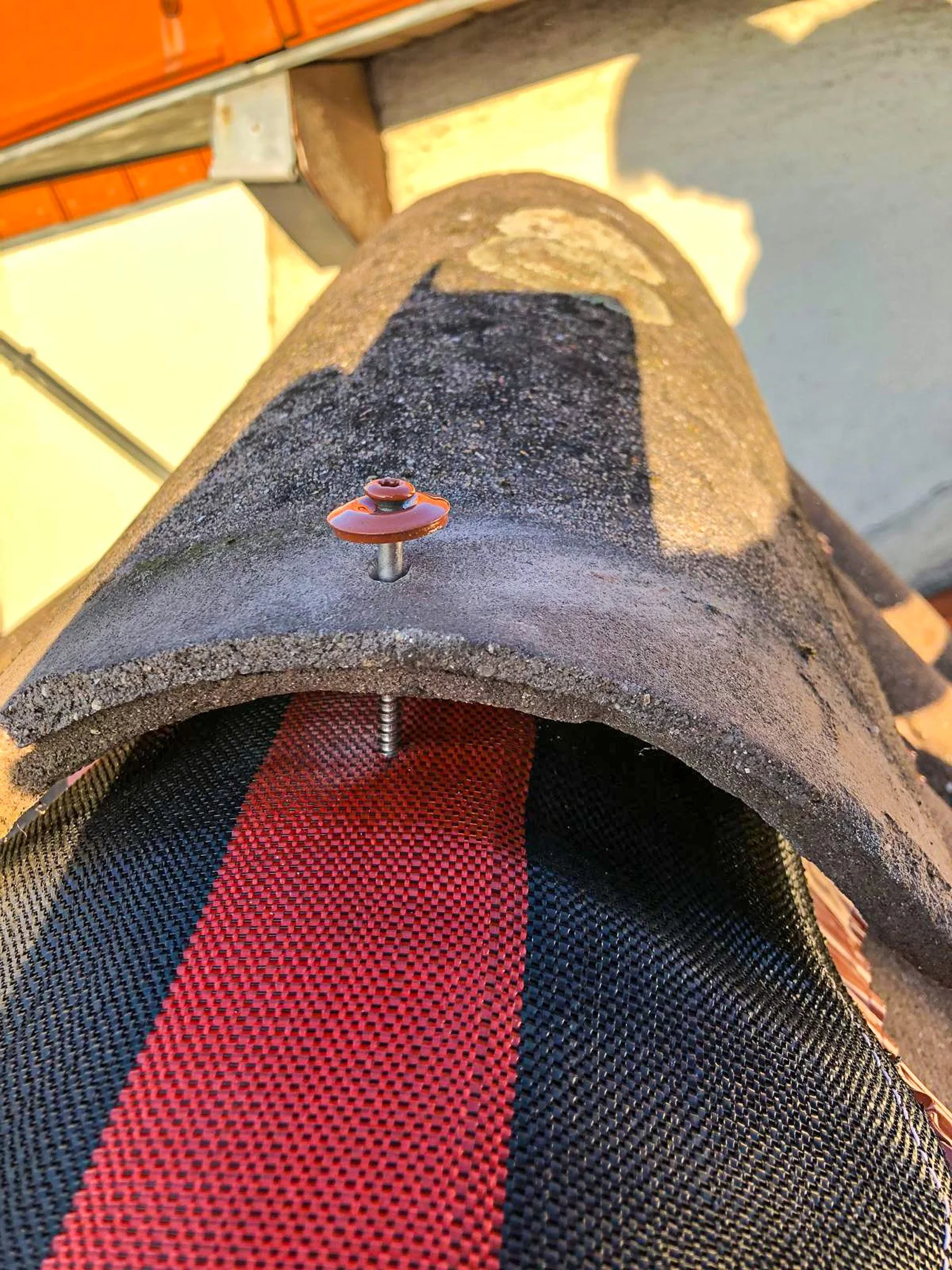 Une vue en plongée d'un tuyau en béton avec un tapis rouge et noir placé à l'intérieur. Sur le dessus du tuyau, il y a une grosse vis de couleur orange.