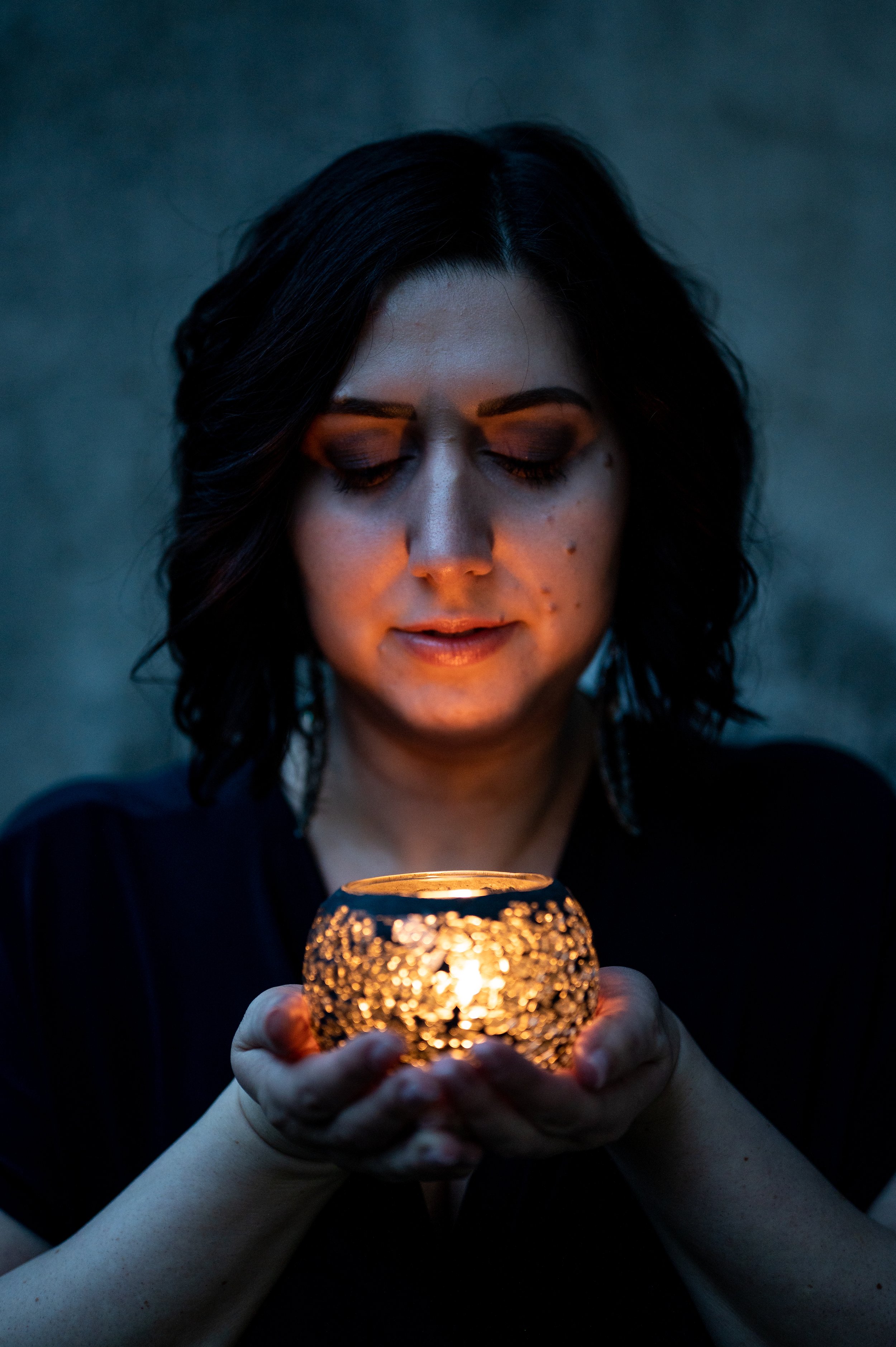 Eine Frau mit dunklen Haaren hält eine kleine Kerze in einer glitzernden Keramikschale, die ein warmes Licht spendet, bei Nacht.