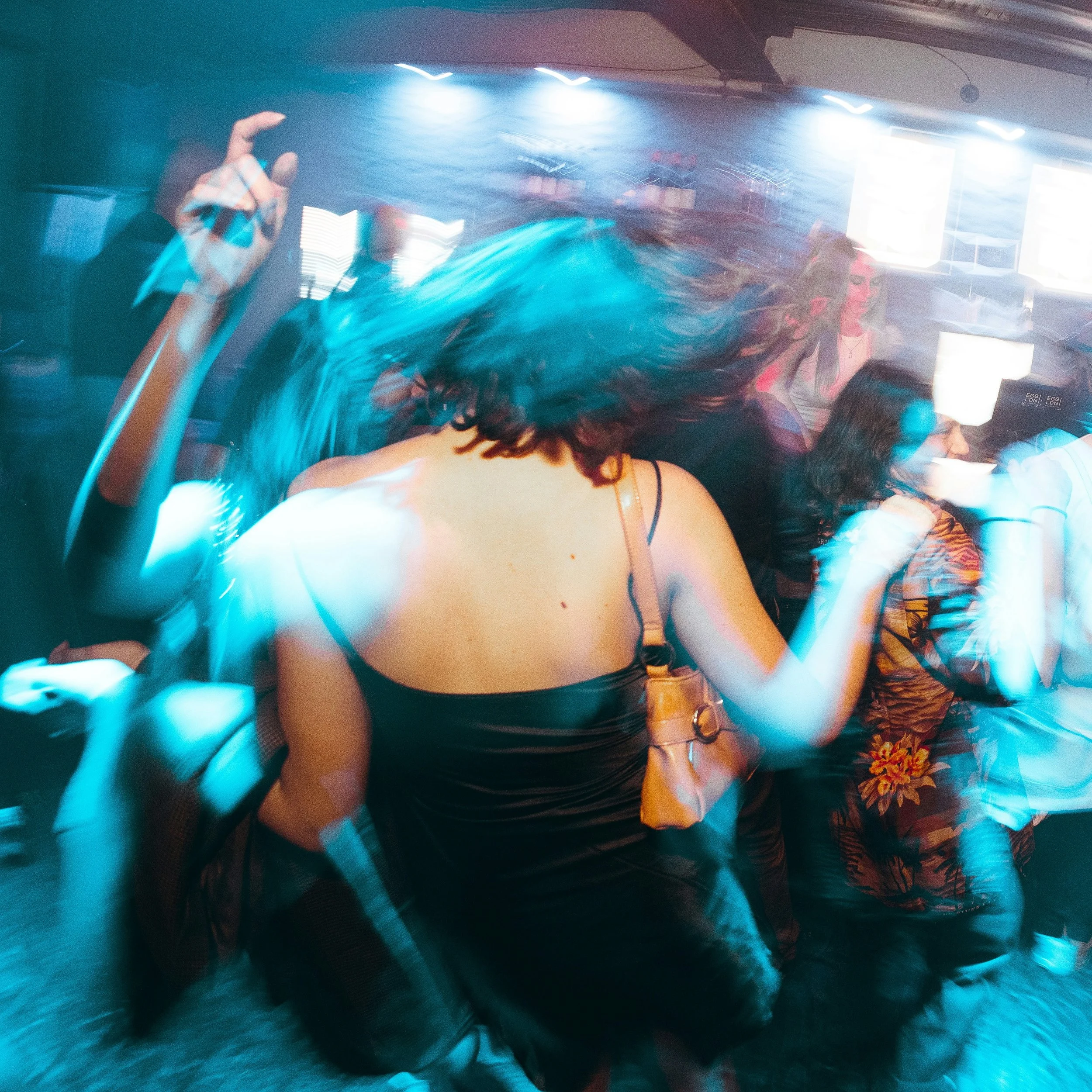Group of women dancing at a nightclub with colorful lighting and motion blur.