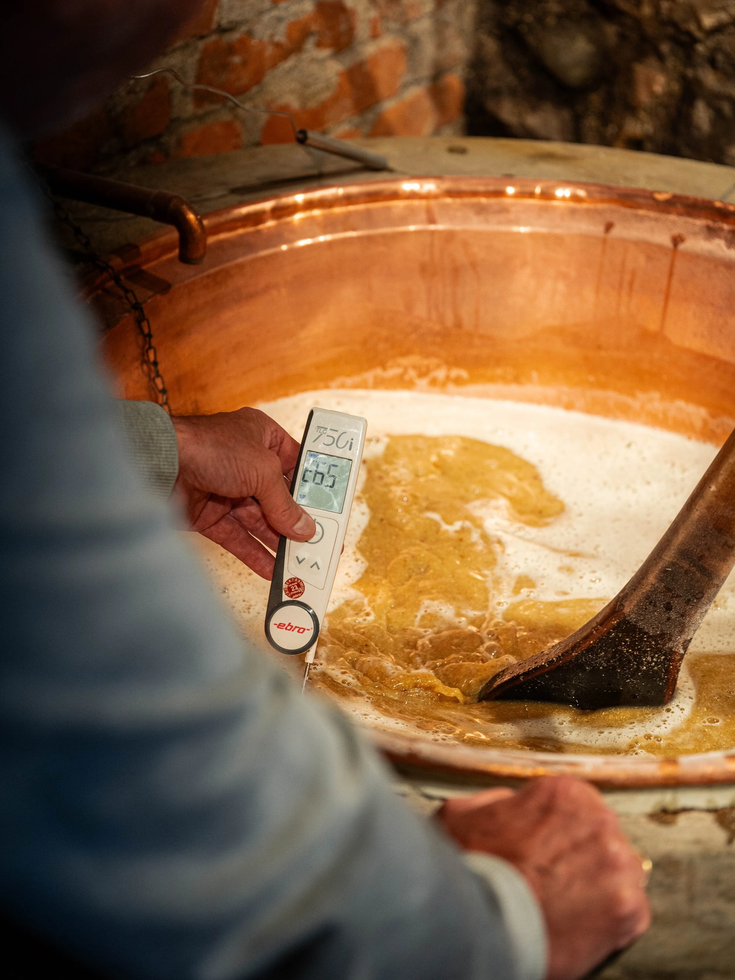 Person misst mit einem Thermometer die Temperatur einer Masse in einem großen Kupferkessel während Braukurs in Salzburg