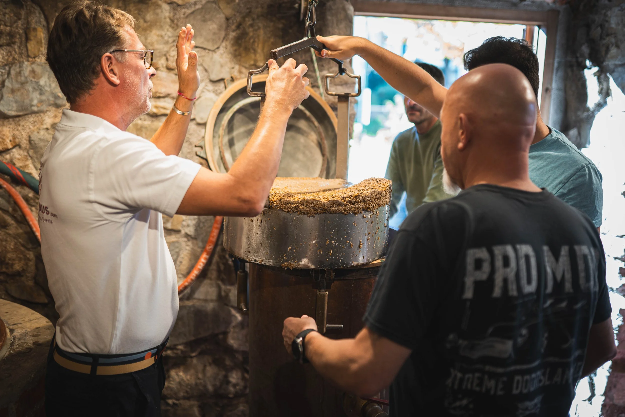 Vier Männer, die eine Trüffel suchen und ernten, während einer mit einem Werkzeug im Boden arbeitet, in einem Steinraum mit Feuerstelle und Steinmauer im Hintergrund.