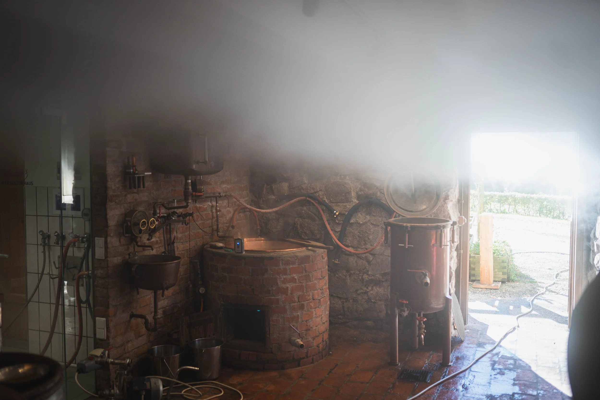 Brauerei mit alten Brühkesseln und Kupferrohren, Blick in den Außenbereich bei hellem Sonnenlicht.
