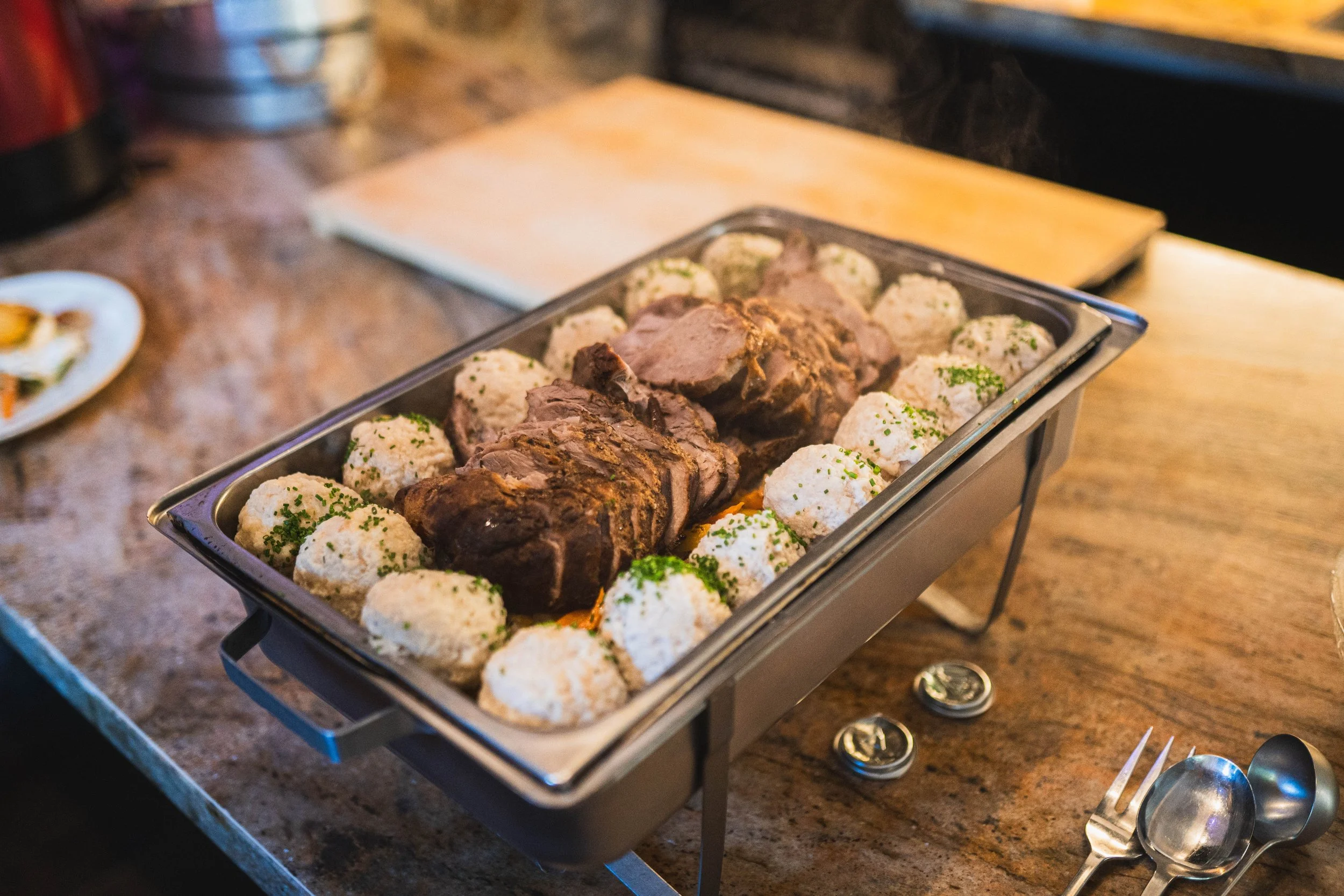 Aufwärmgericht mit Schmorbraten umgeben von Kartoffelknödeln auf einem Edelstahlwärmeteller.