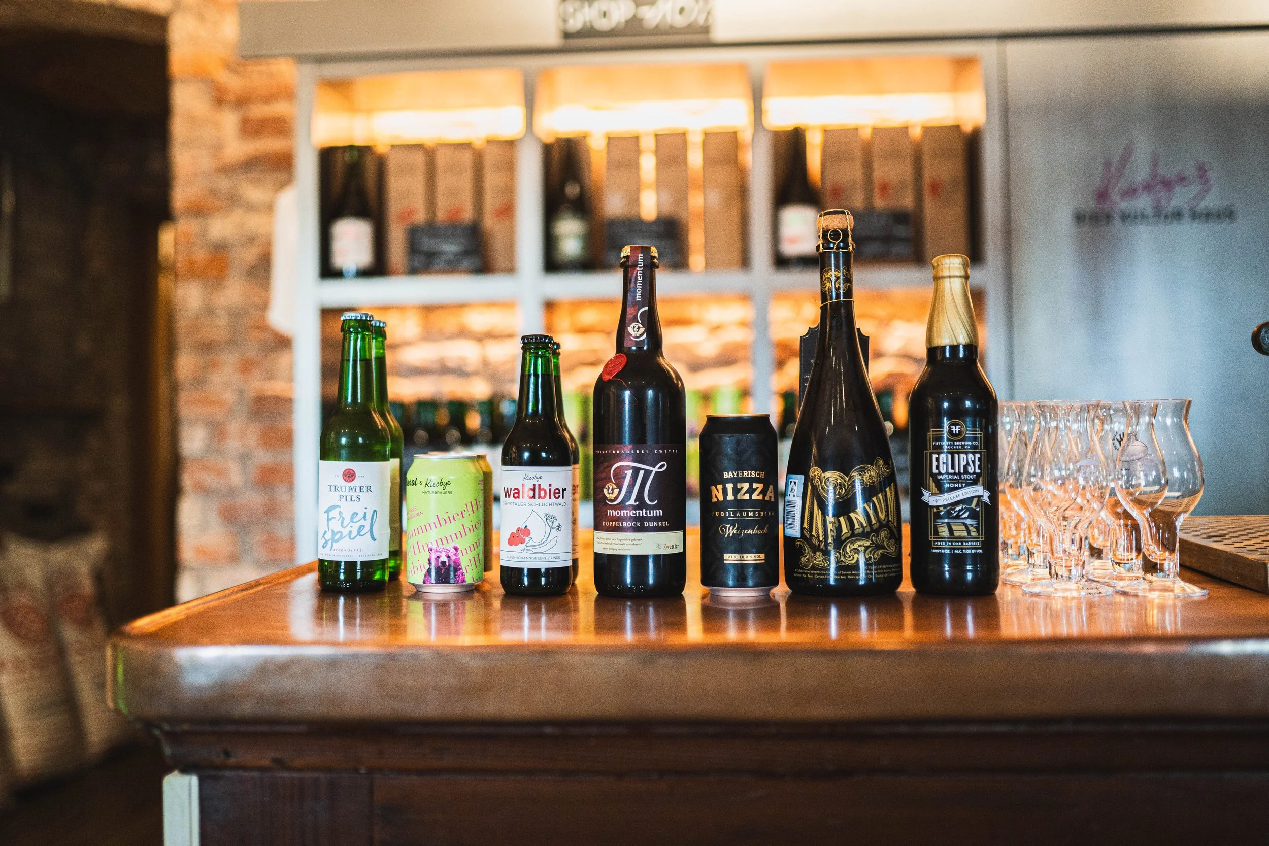 Verschiedene Flaschen Bier und Biergläser auf einem Holztheken in einer Bar