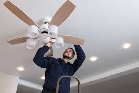 A man standing on a ladder installing or fixing a ceiling fan with lights.