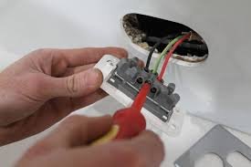 Hand using a screwdriver to connect wires to a circuit breaker in an electrical outlet.