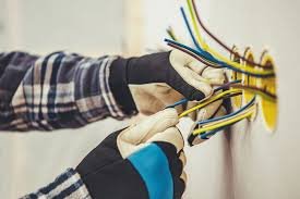 A person installing or repairing electrical wiring in a wall, wearing gloves and using tools to organize and connect wires.
