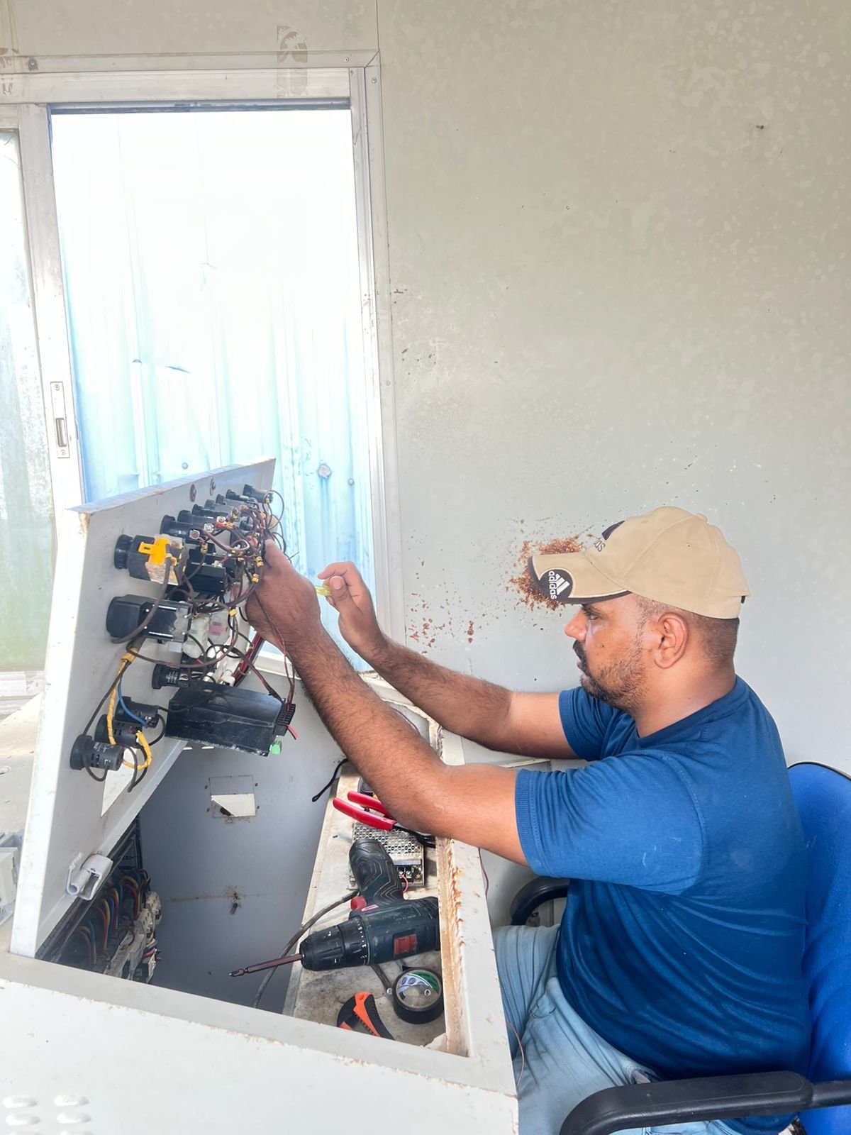 A man using tools like a power drill, with tools and wires on a work surface nearby.