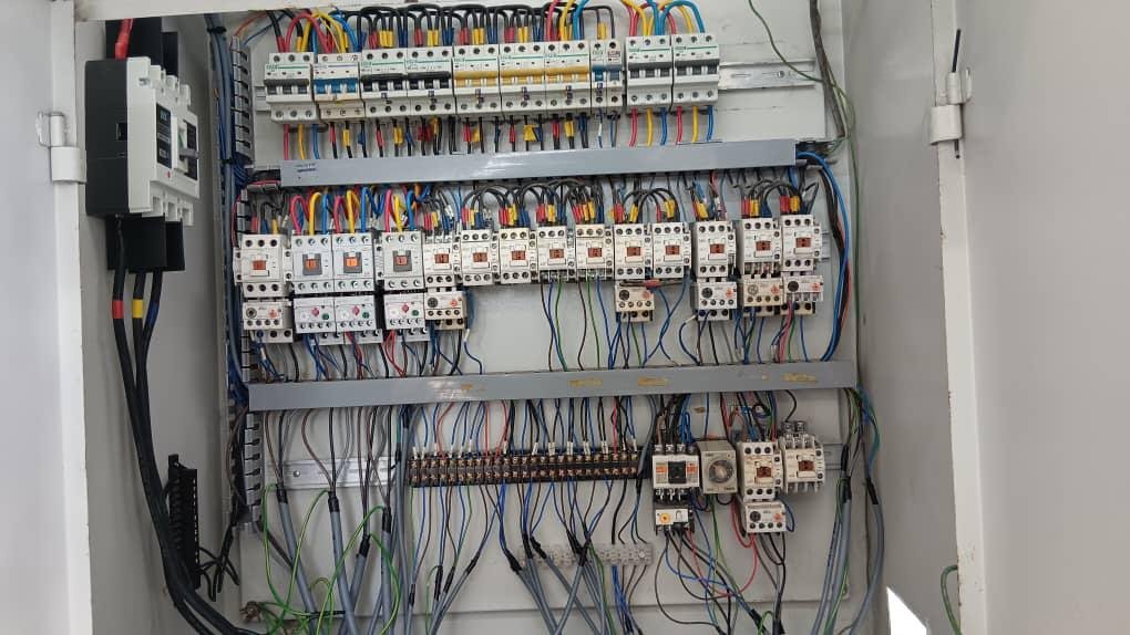 Electrical panel with multiple circuit breakers, wires, and connectors organized on a gray metal board inside a cabinet.