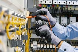An electrician wearing gloves working on a row of electrical switches and wiring.