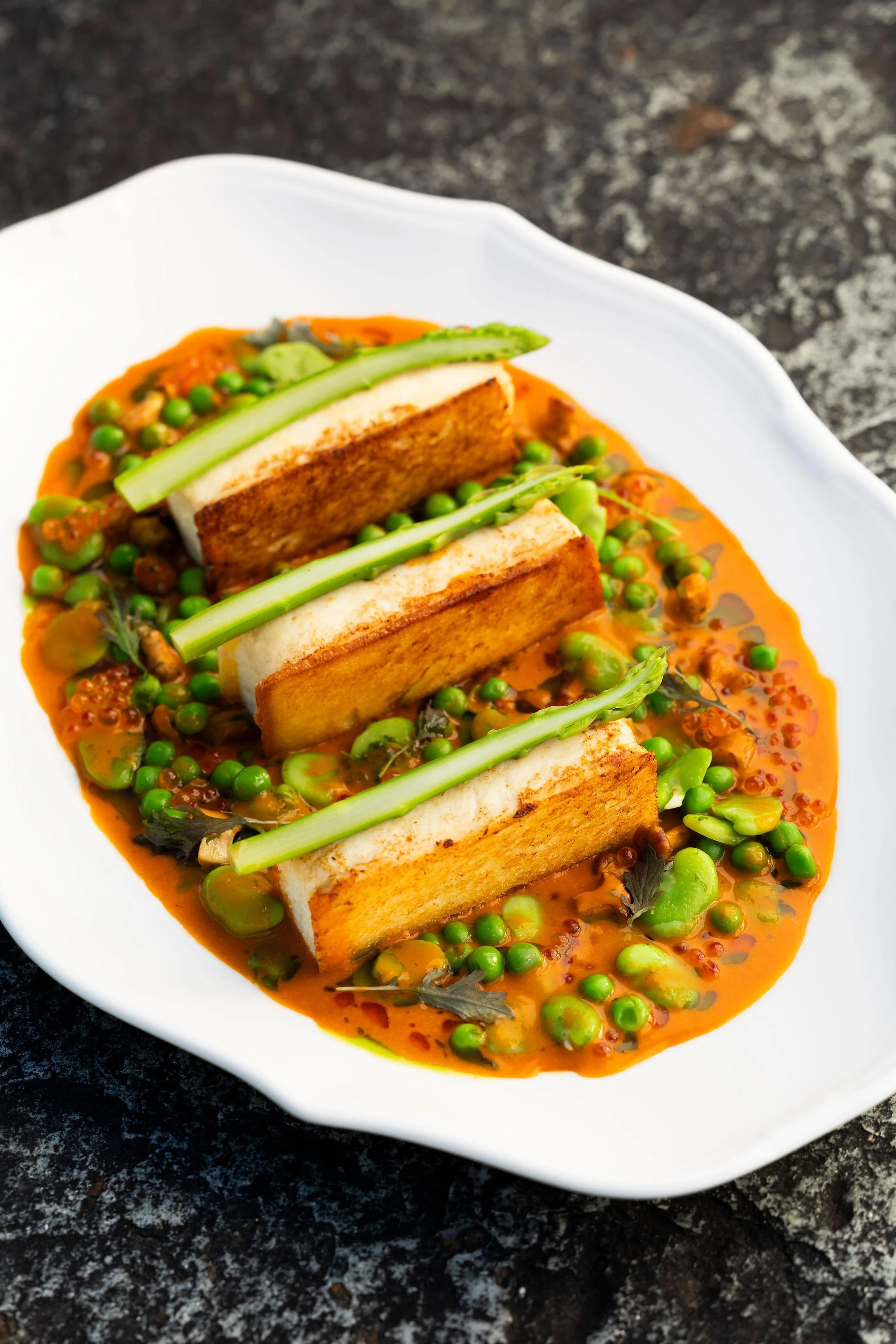 Tartines de pain avec sauce aux légumes verts et pois, décorées de brins de céleri, dans une assiette blanche.