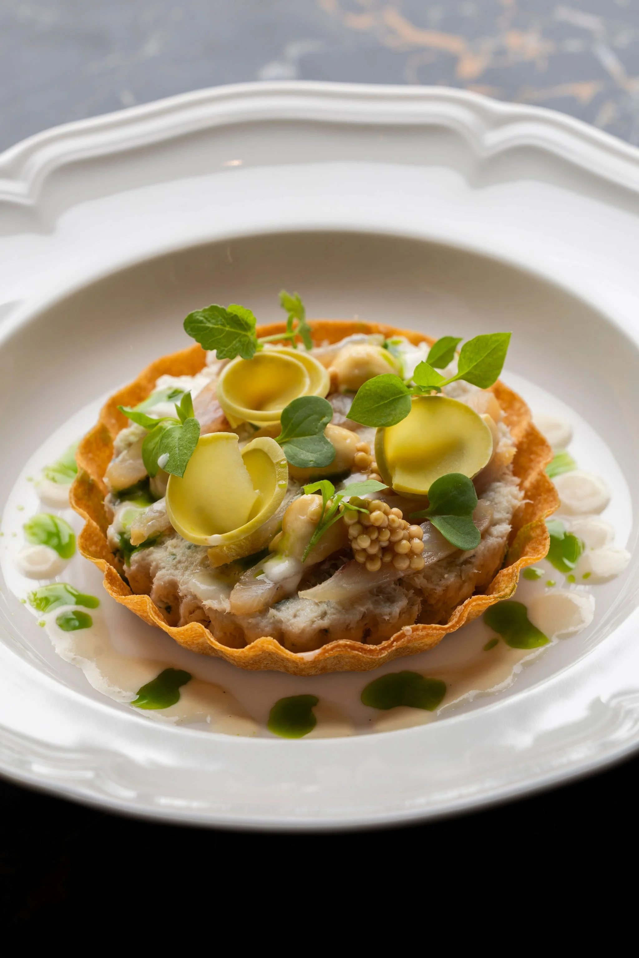 Tartelette avec légumes, herbes et sauce sur une assiette blanche