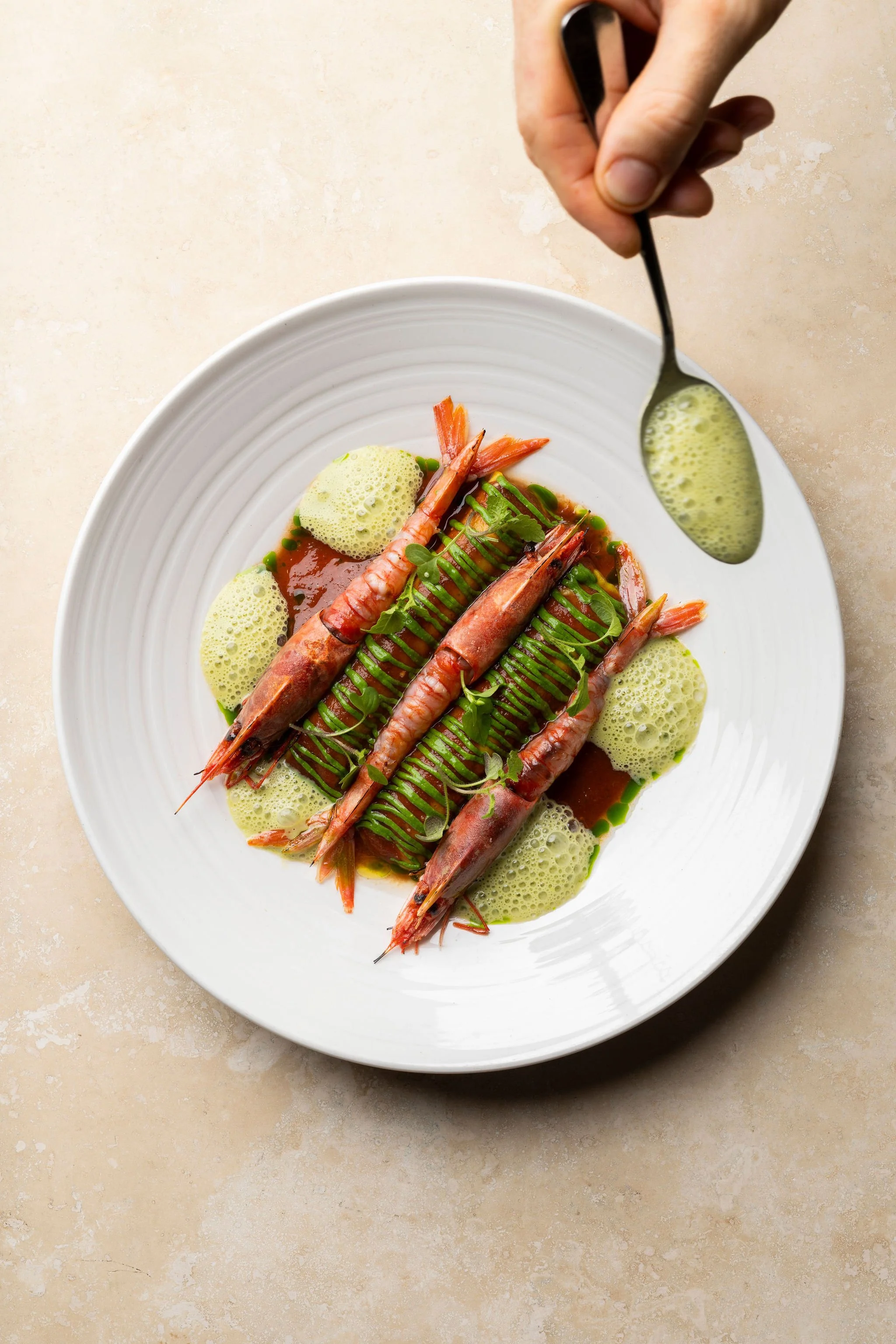Une assiette de gamberro rosso, avec une sauce verte, des mousses jaunes, et des herbes, vue du dessus.