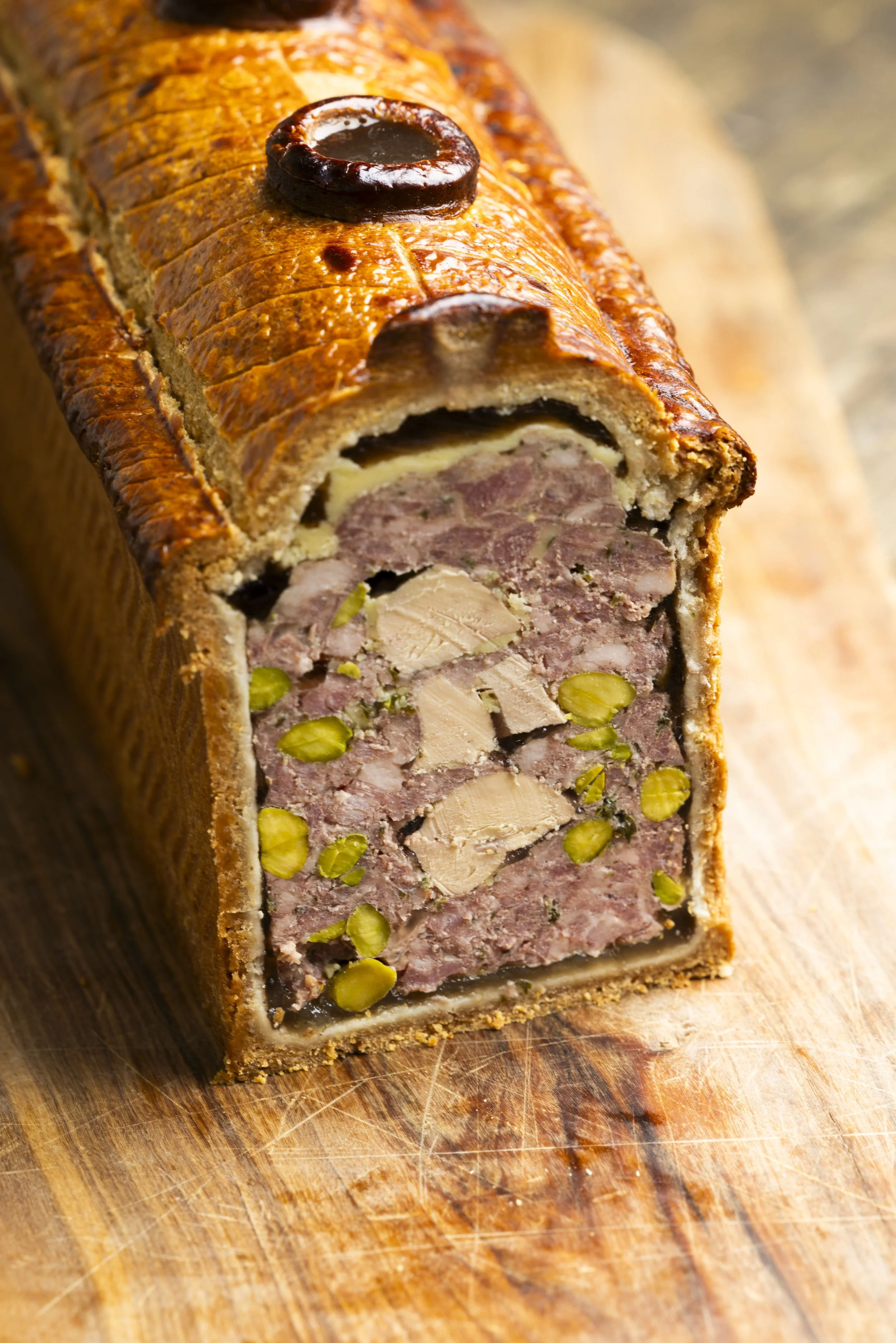 Pain de viande en croûte avec une garniture de pistaches, présenté sur une planche en bois.